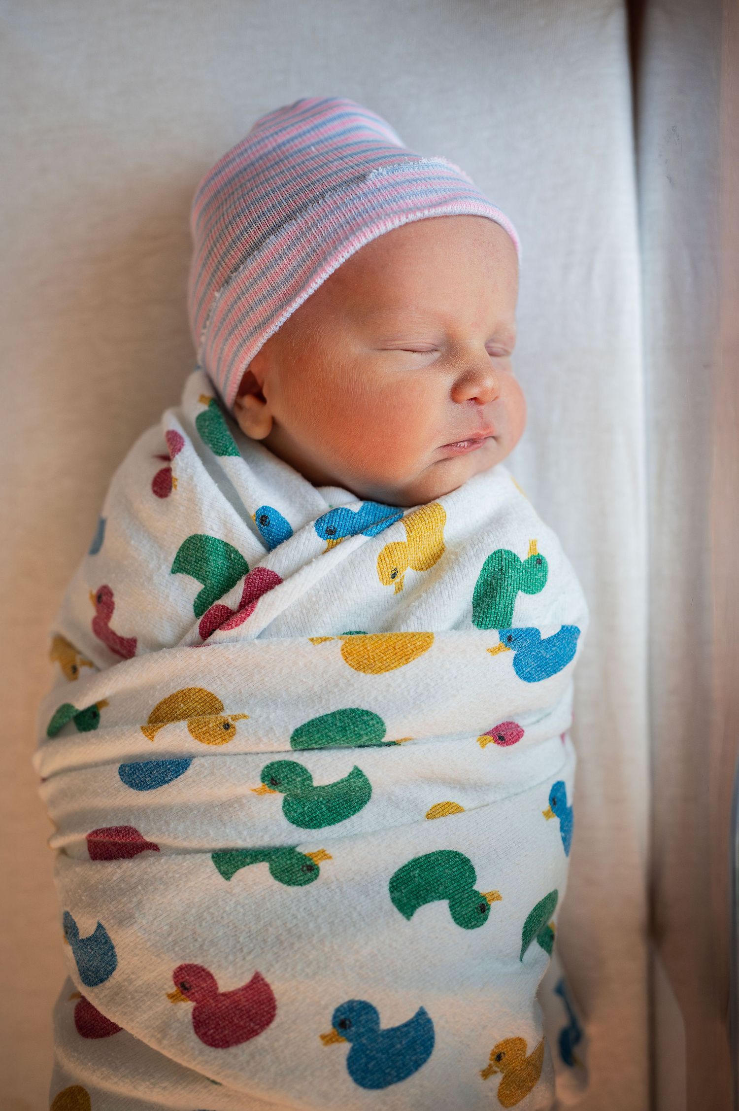Newborn swaddled in a rubber duck blanket, sleeping under soft window light during a lifestyle session in Columbus.