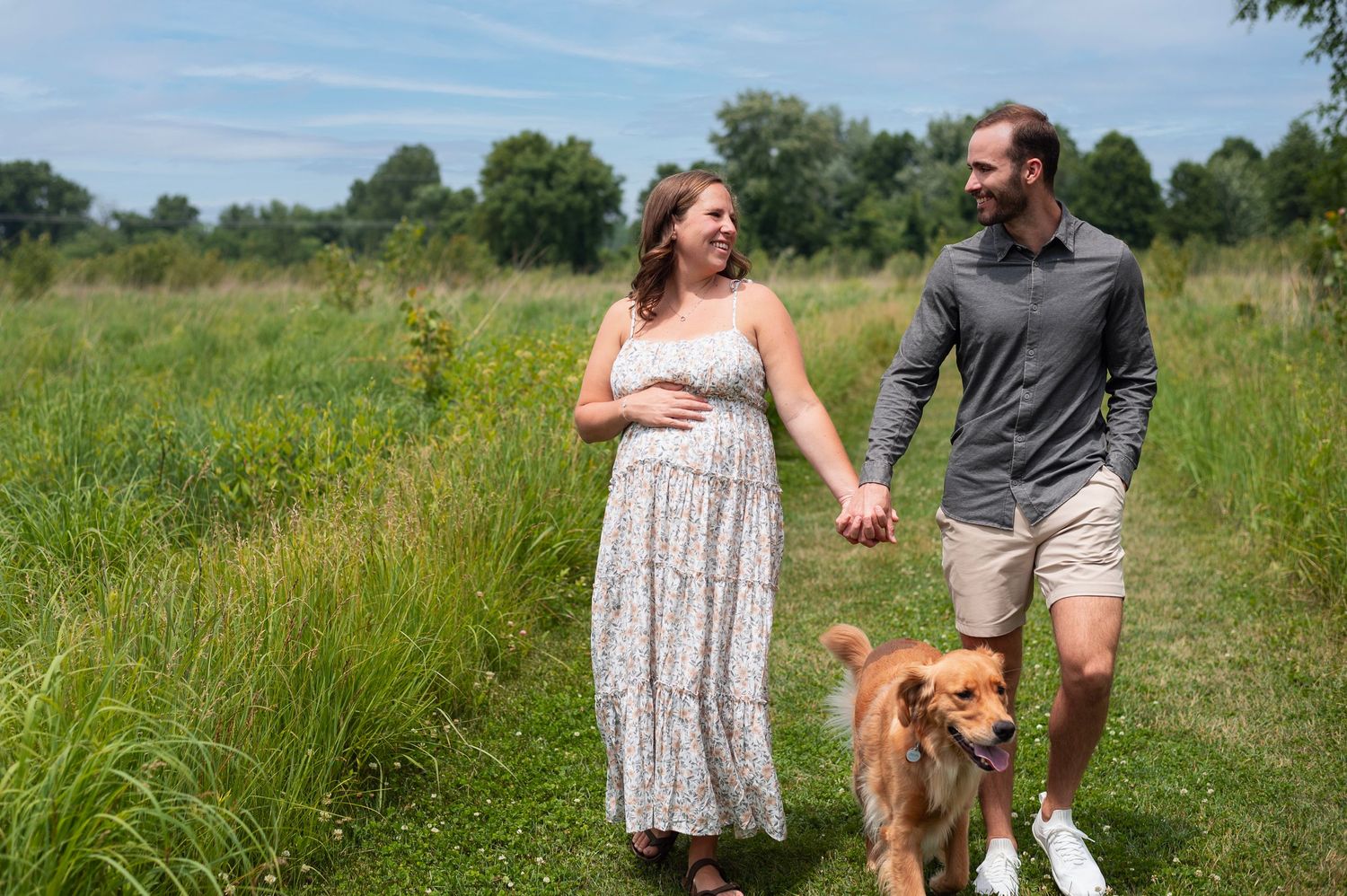 Expecting couple walking with dog through open grassy field at Rocky Fork Metro Park maternity session.