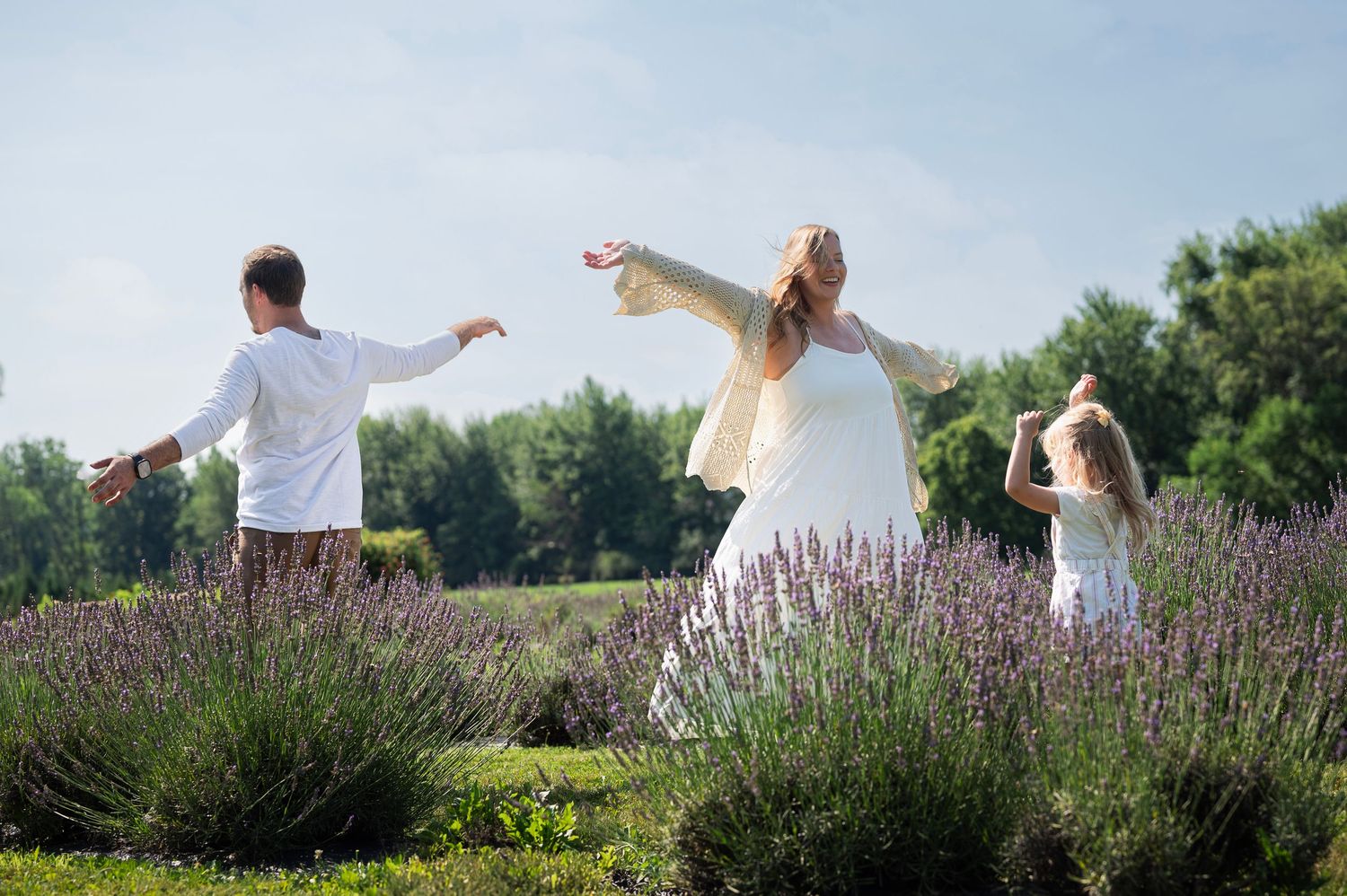 Family dancing and spinning in a lavender field on a sunny day, wearing light, airy clothing.