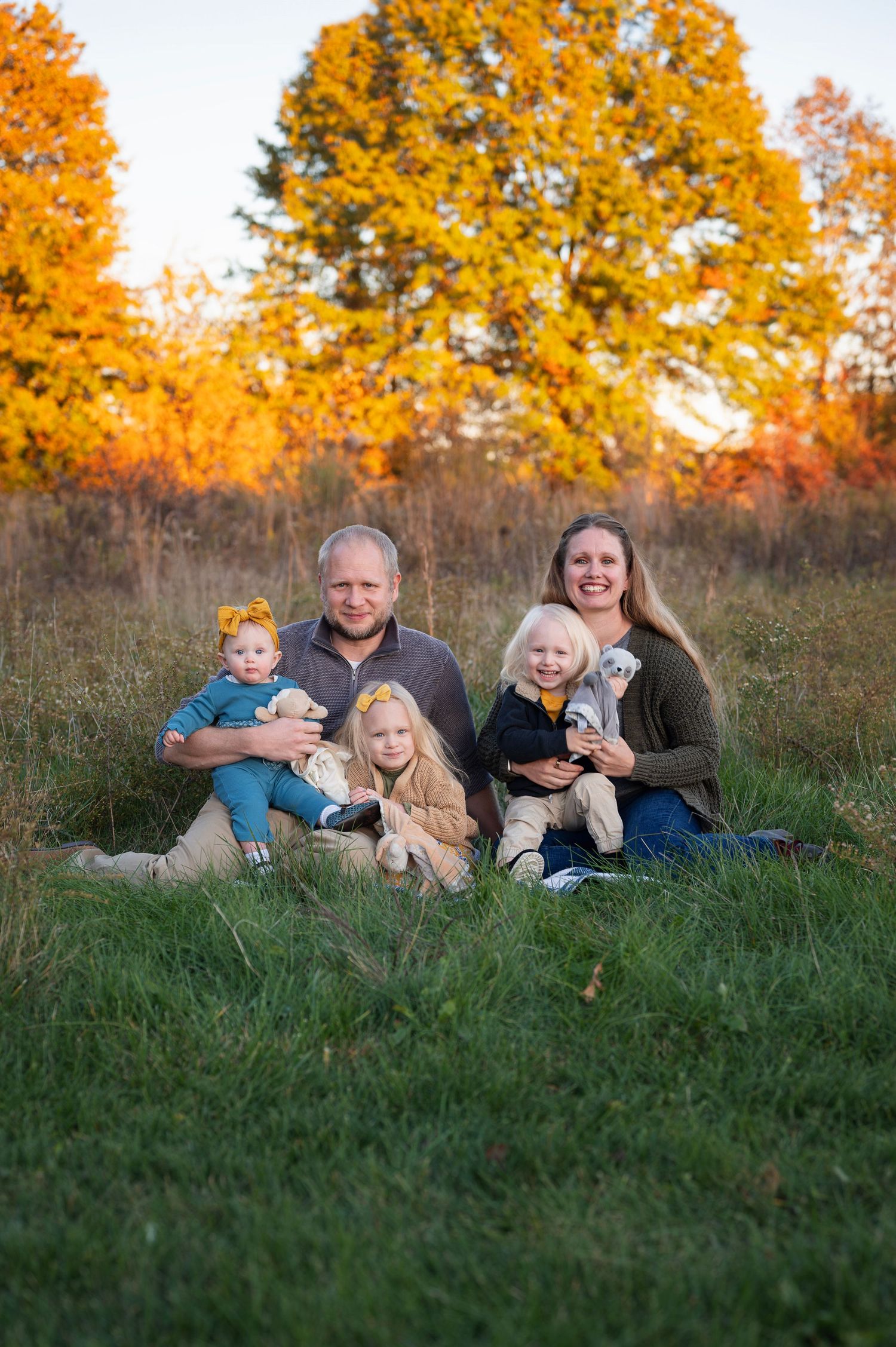 Fall family photo with three young children in cozy neutral outfits, taken during golden hour in a grassy field.