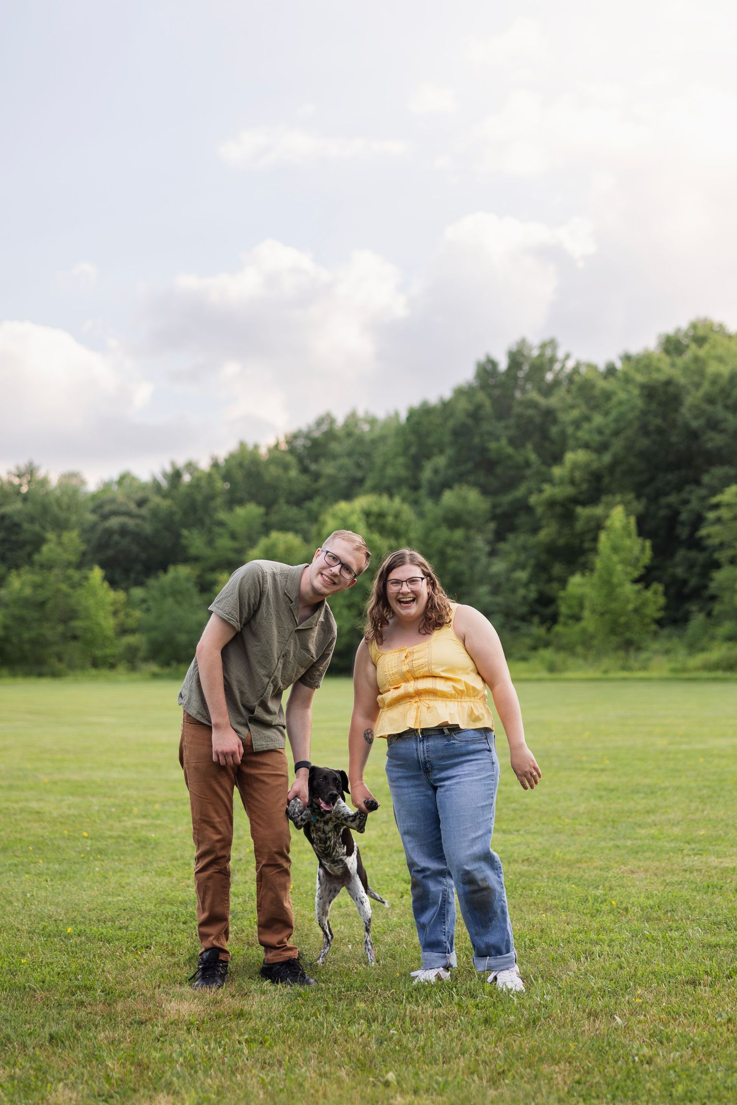 Smiling couple in a park with their playful dog during a relaxed outdoor family photo session.