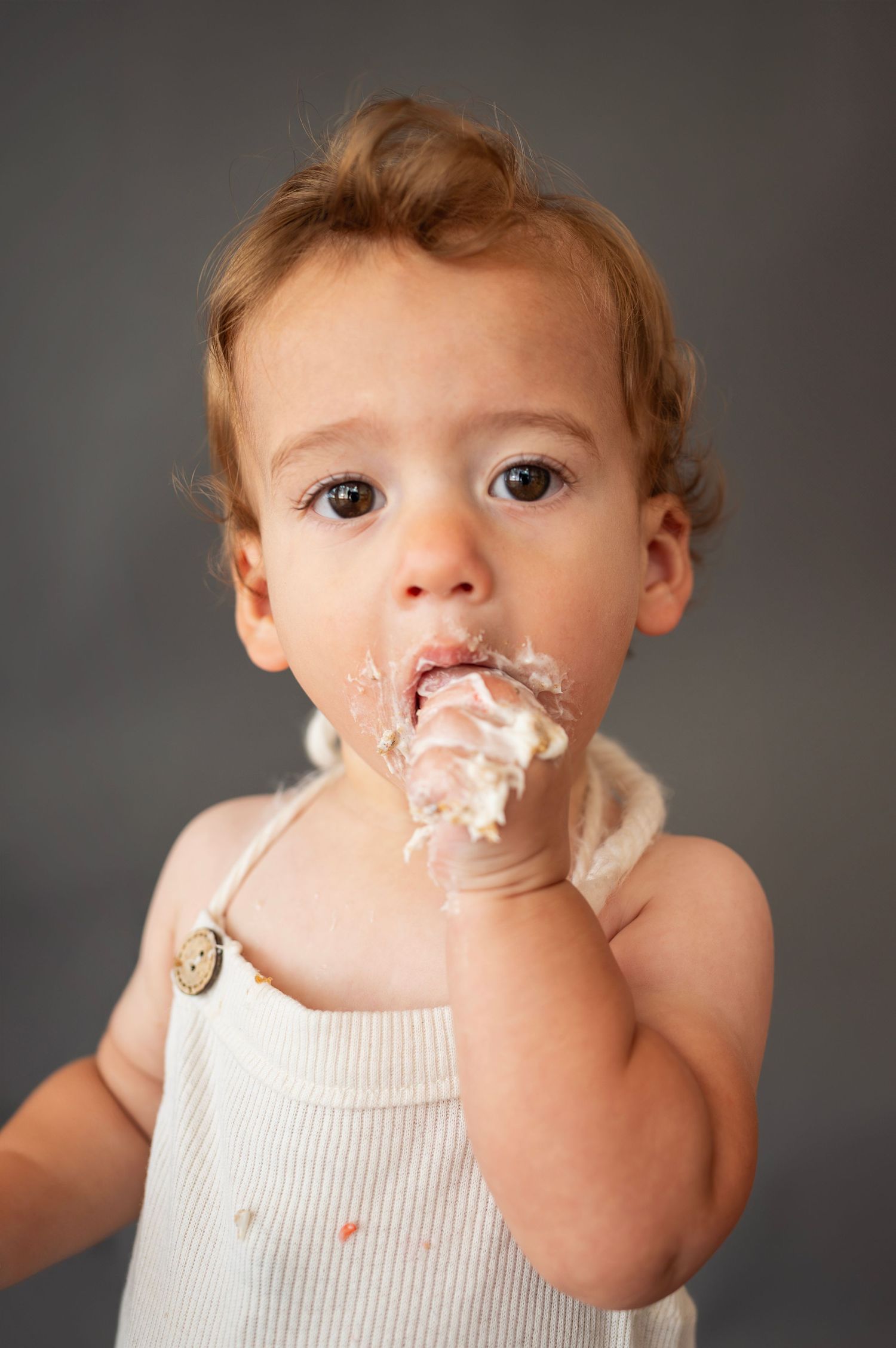 Toddler reaches out with both hands while covered in frosting during an indoor cake smash session.