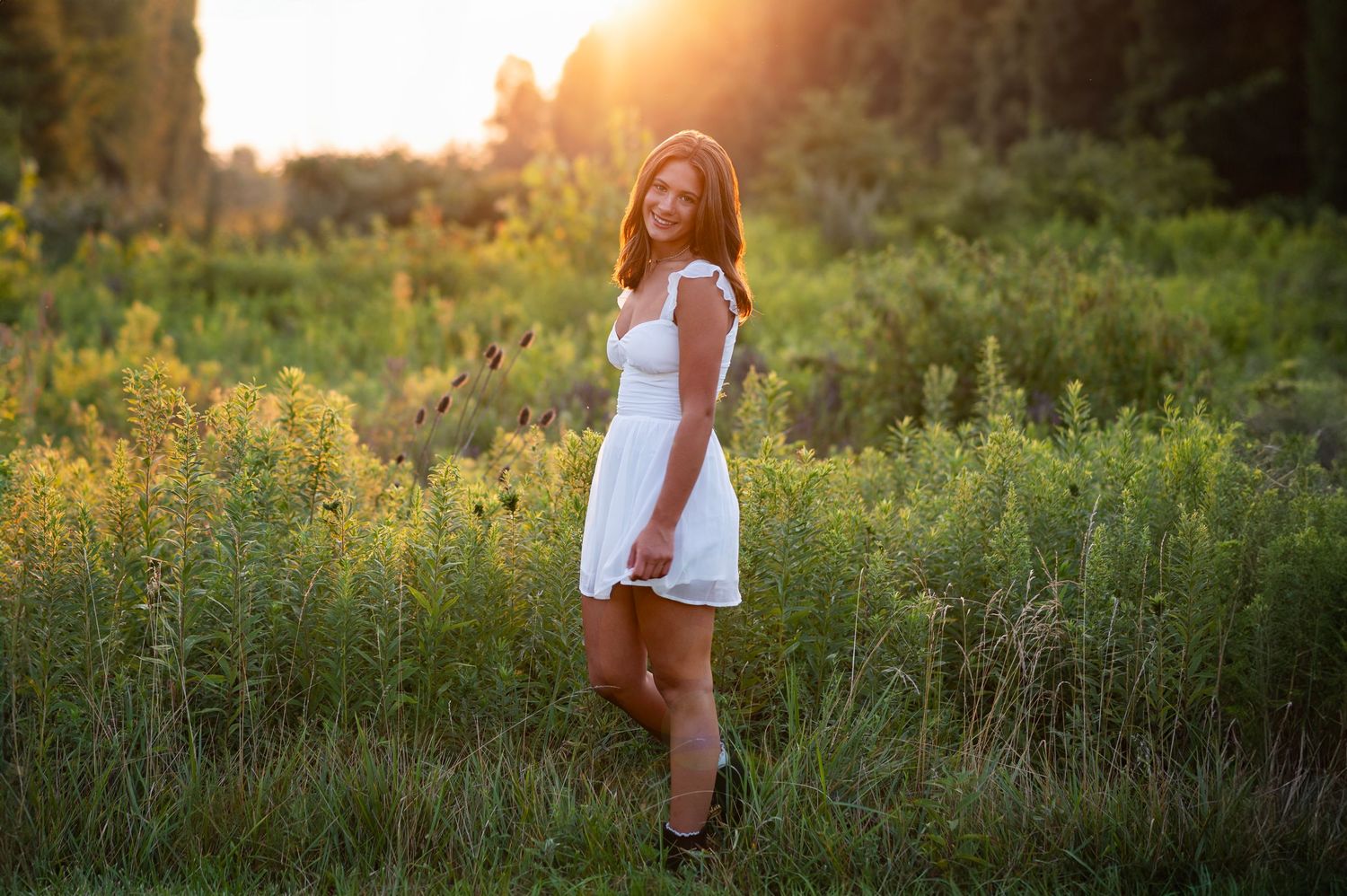 Teen girl in a white dress standing in a tall grassy field at sunset, smiling over her shoulder. Rocky Fork Metro Park