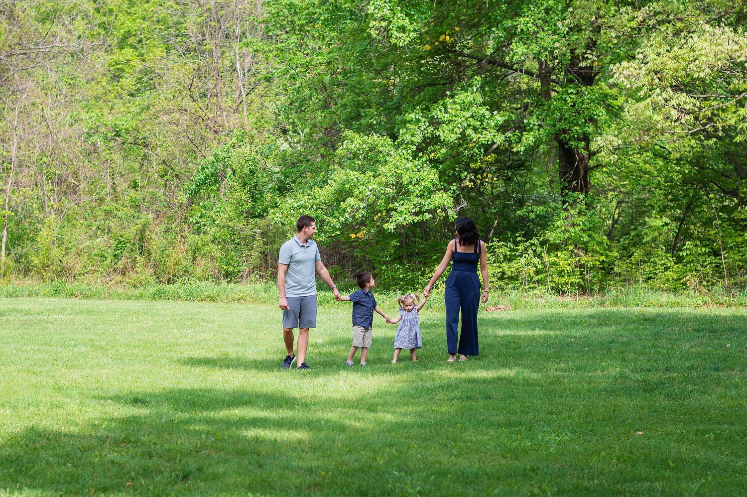 Family of four walks hand-in-hand through the grass during a relaxed, child-led photo session at Highbanks Metro Park.