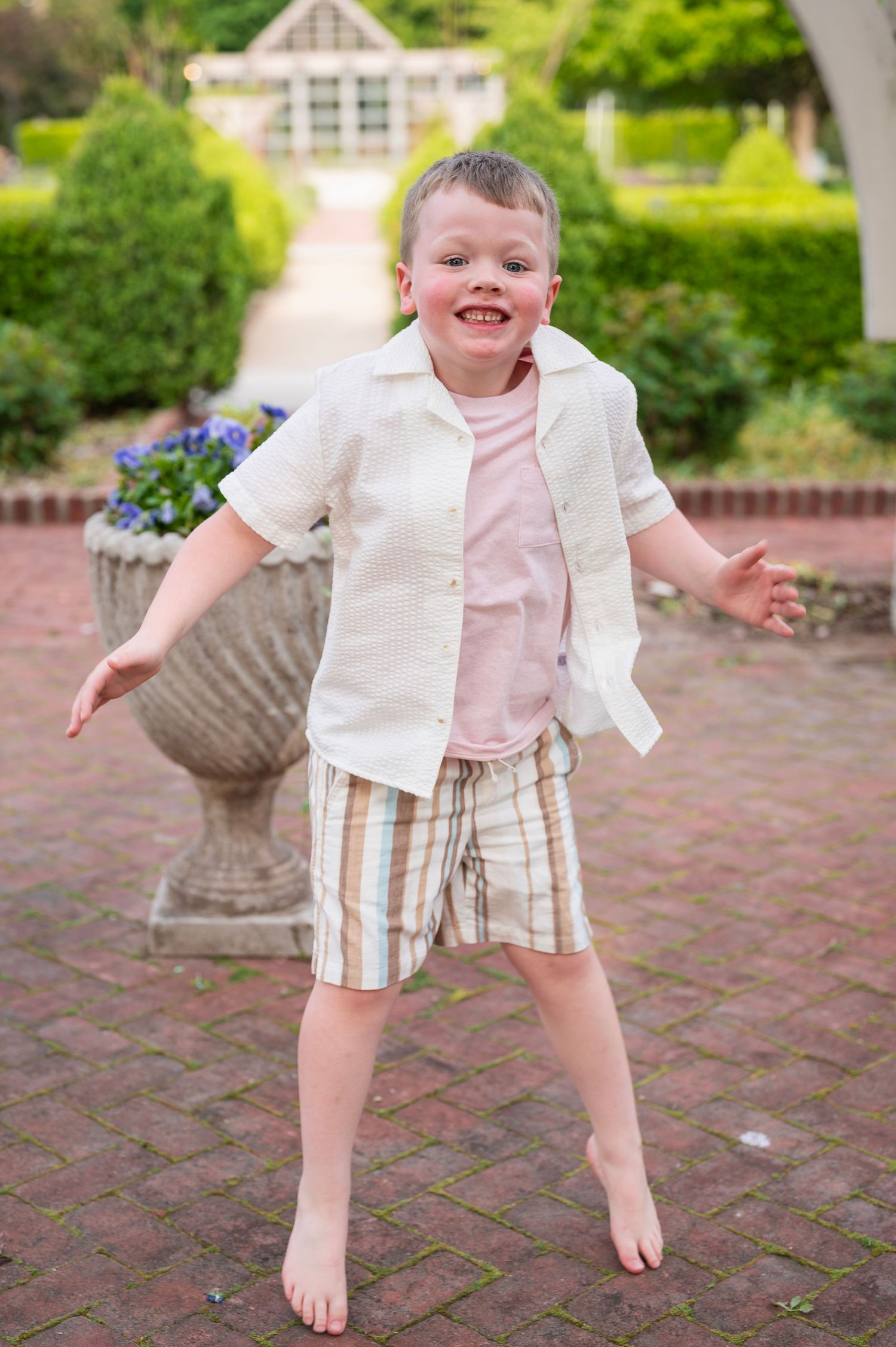Barefoot boy mid-jump with a big smile during a playful family photo session in a Columbus garden.