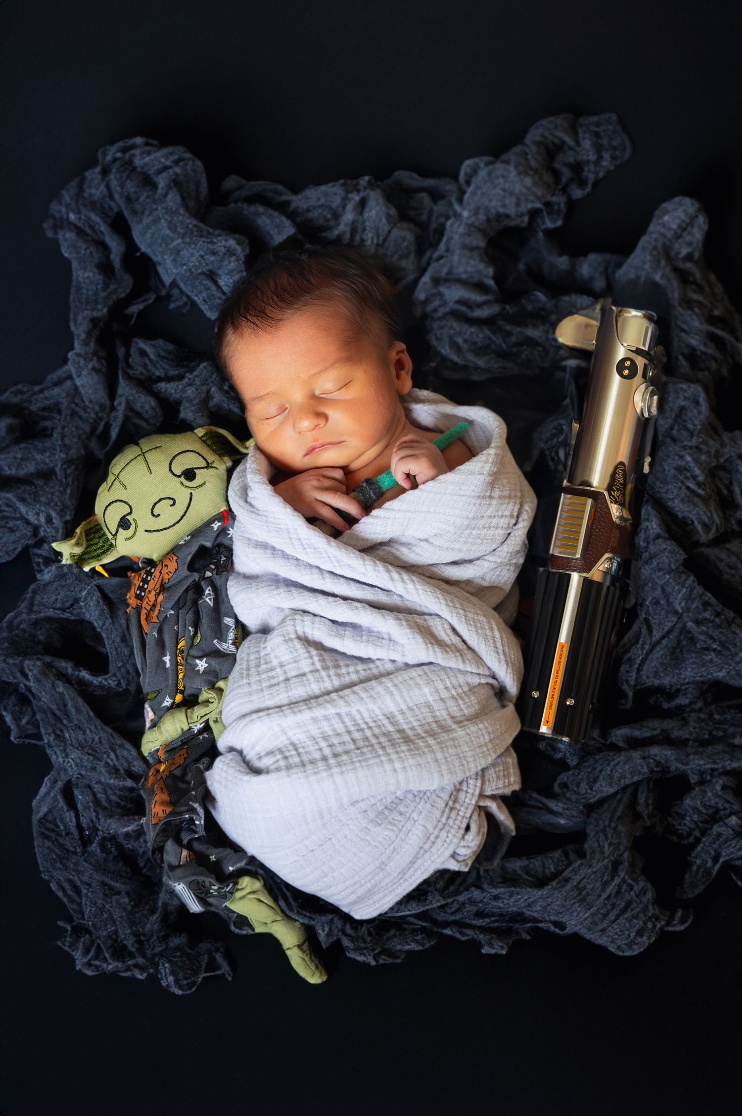 Star Wars-themed newborn session with baby swaddled between a Yoda plush and lightsaber.