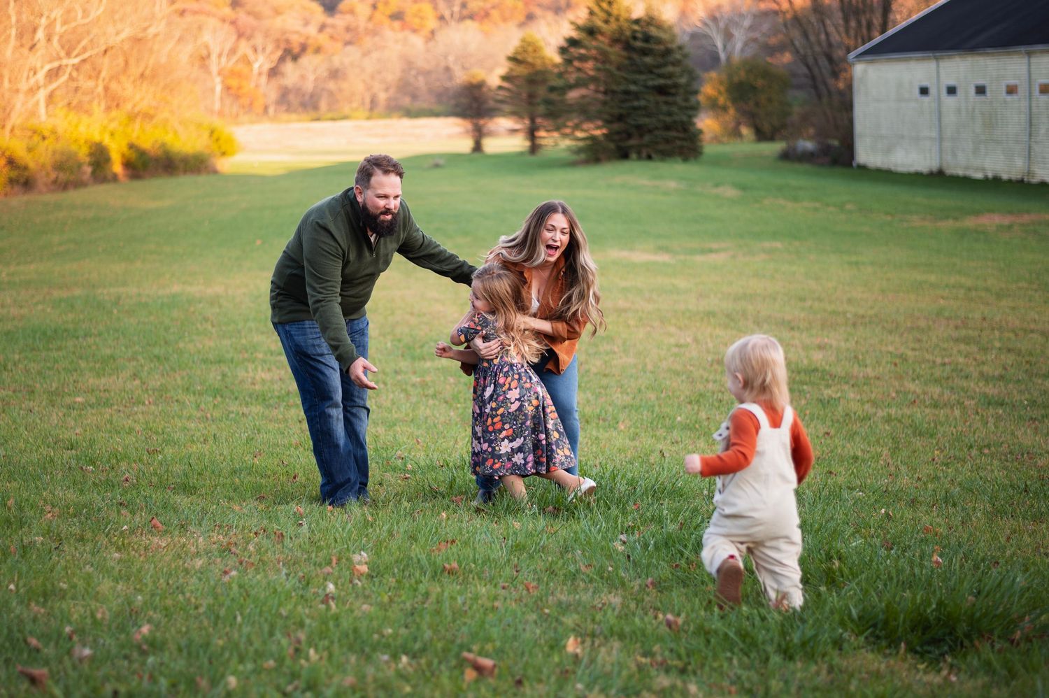 Parents playing in field with two kids during golden hour, candid fall family session near Columbus.