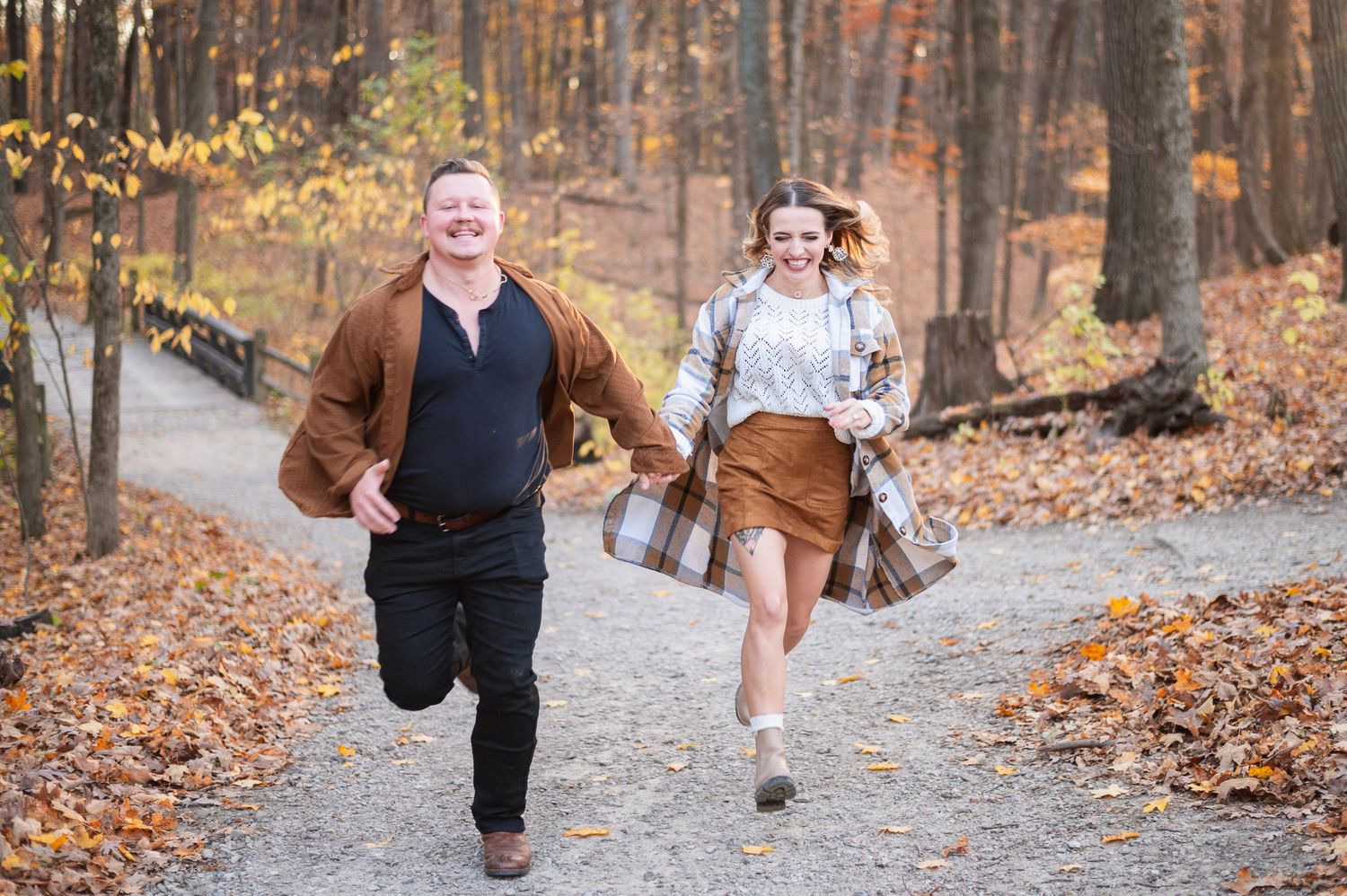 Couple running hand in hand on a leaf-covered trail at Highbanks Metro Park in Columbus.