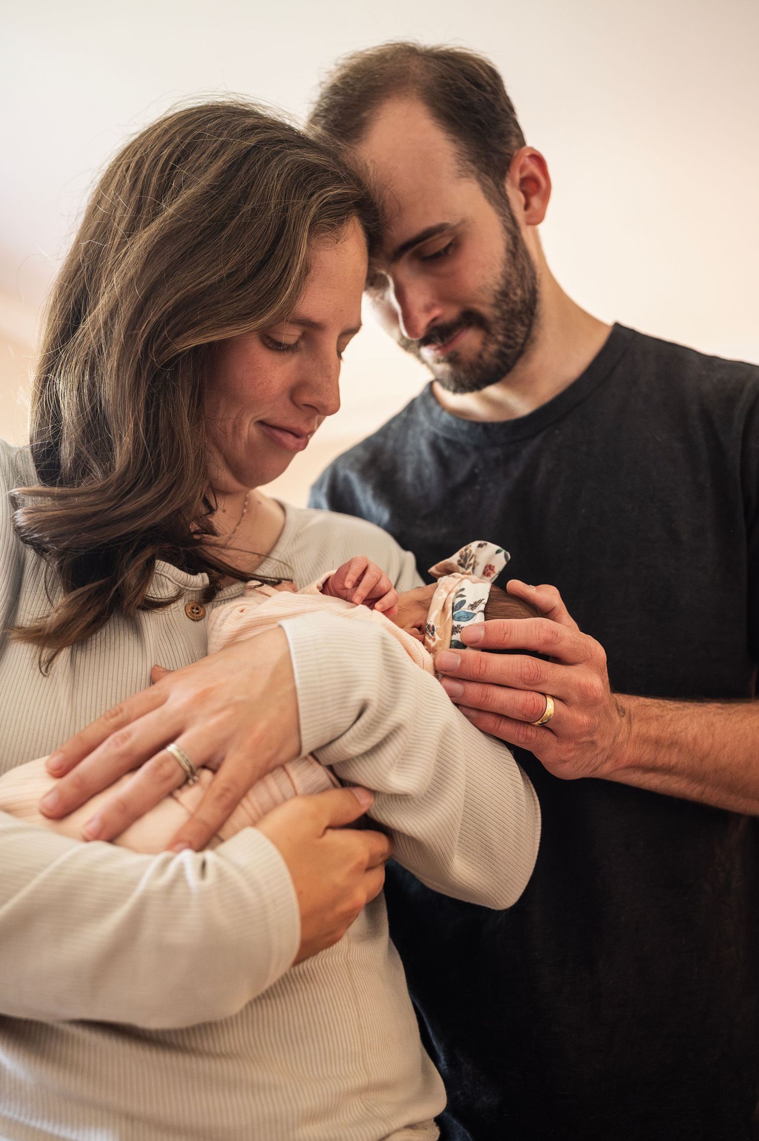 Tender moment of new parents holding their newborn daughter together in soft indoor light.
