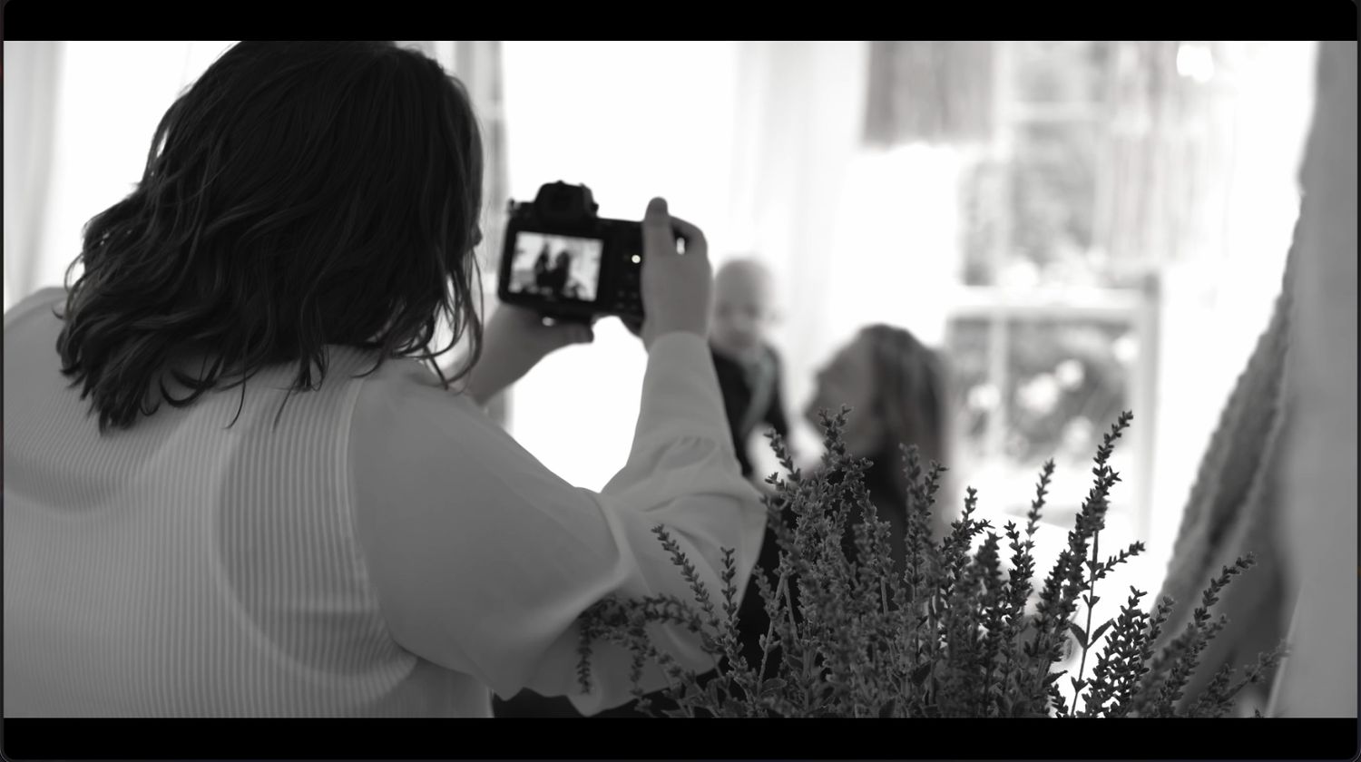 Photographer holding camera, capturing candid family moments during an indoor session in natural light.