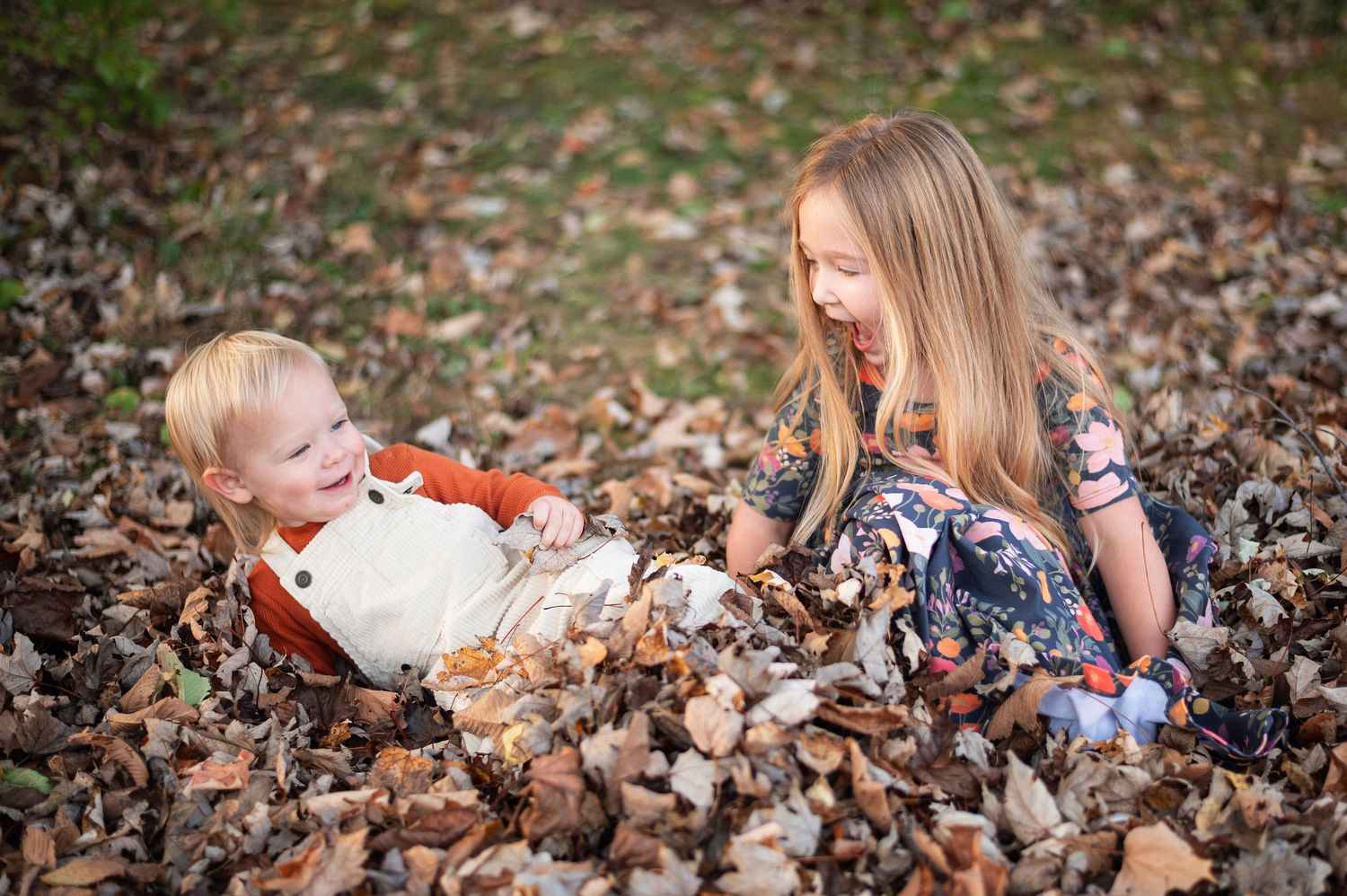 Brother and sister laughing in a pile of fall leaves—Westerville milestone photography session