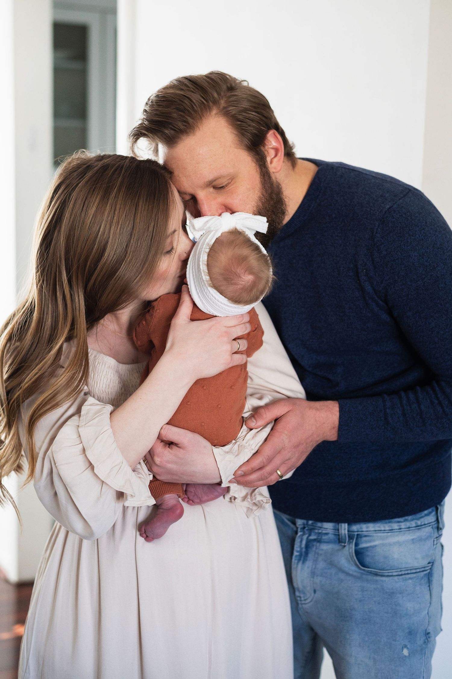 Mom and dad kiss their newborn in a quiet moment of love during an in-home newborn photography session in Columbus.