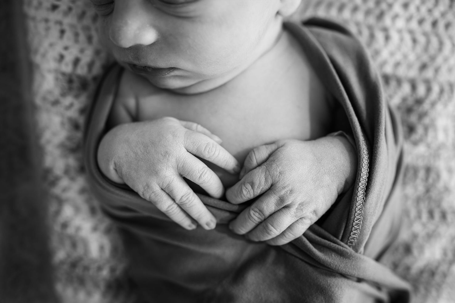 Close-up black and white image of newborn hands wrapped in a blanket—fine art detail from a lifestyle newborn photography session.