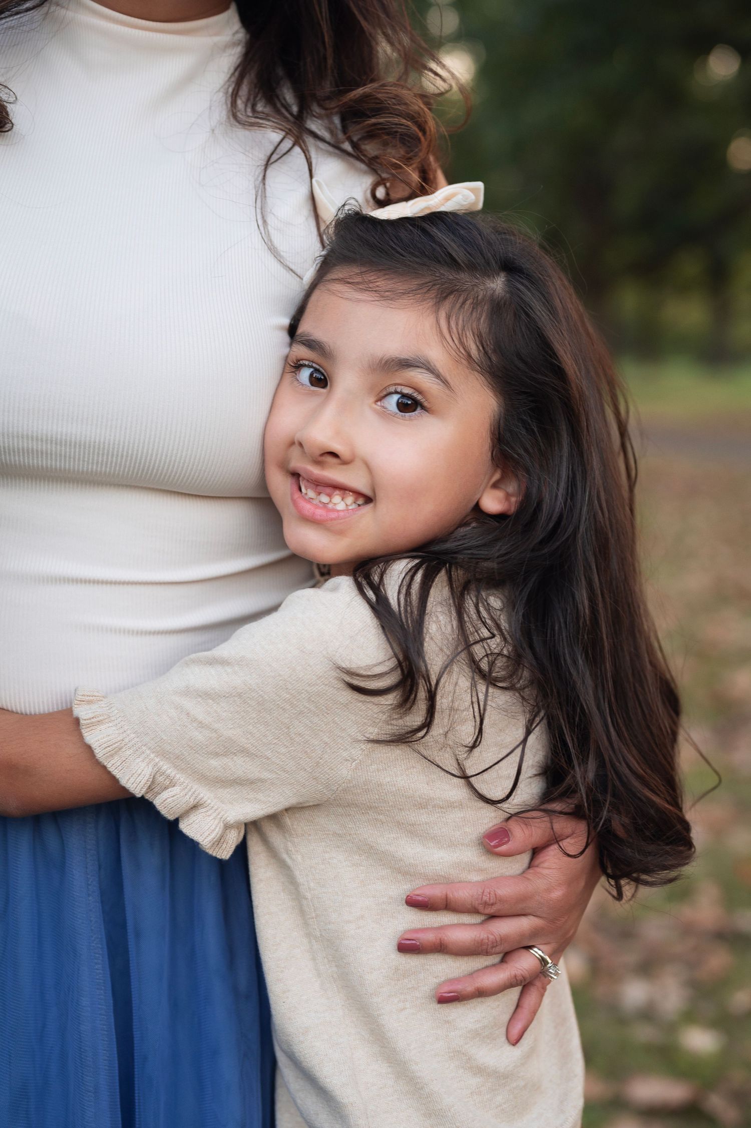 Big sister hugs her mom’s waist on a fall evening at Sharon Woods, smiling at the camera. Westerville family photographer.