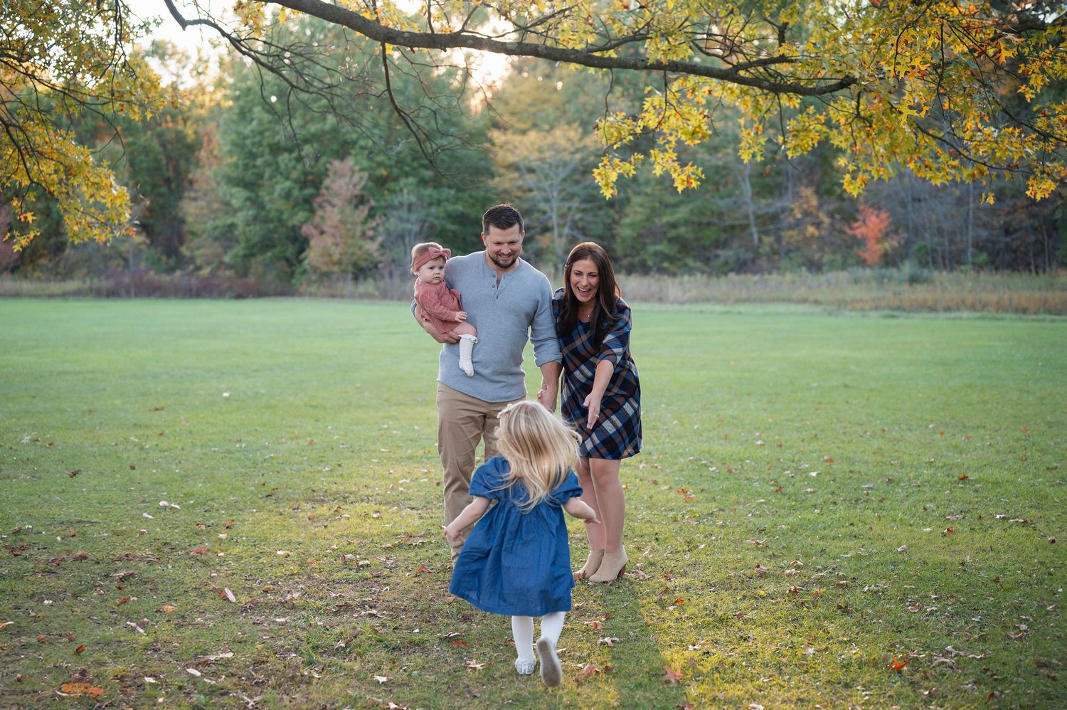 Parents smiling as daughter runs toward them in open field at Sharon Woods Metro Park family session.
