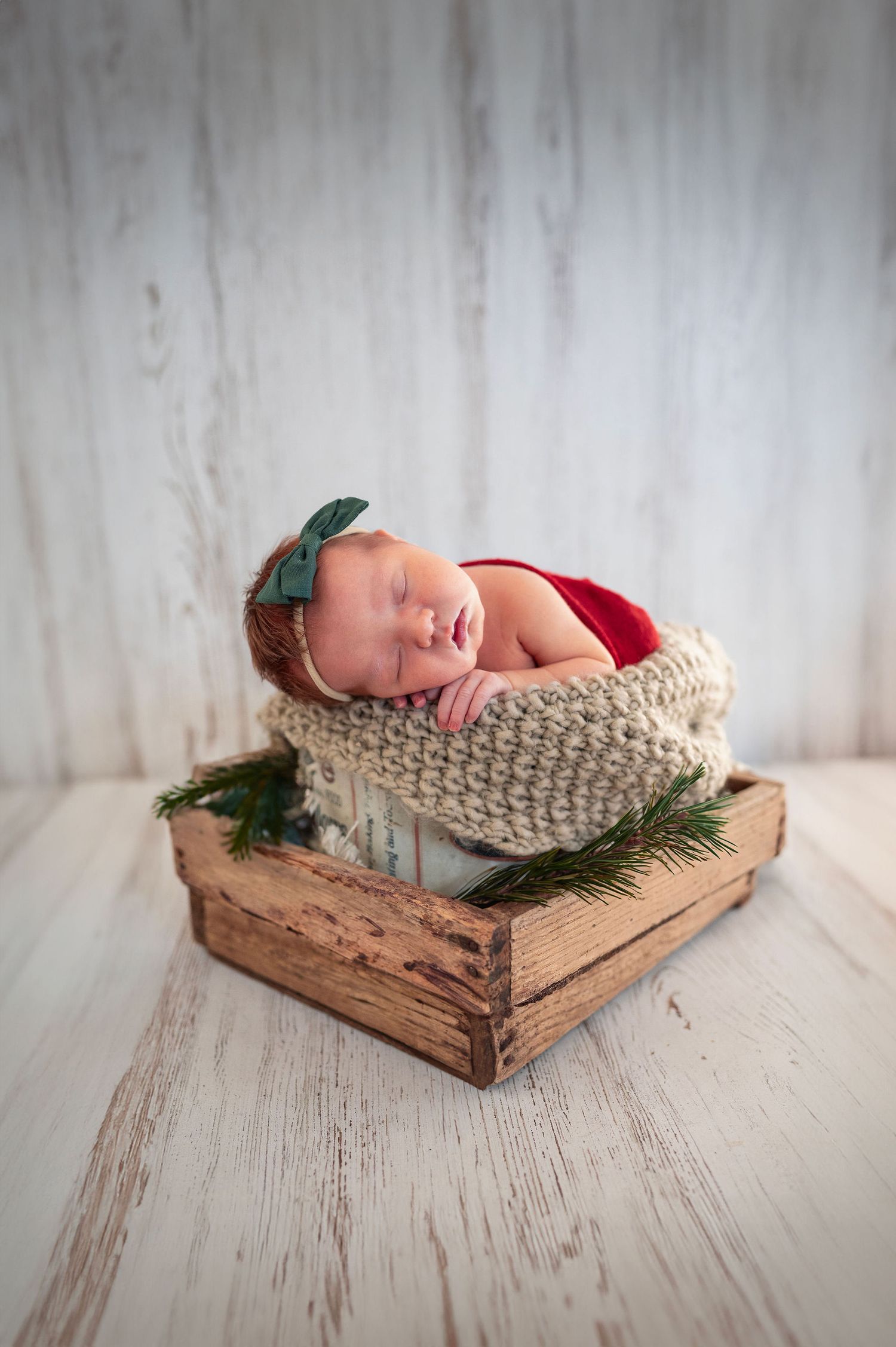 Newborn girl in red and green posed in a studio crate setup during a Westerville newborn studio photography session.