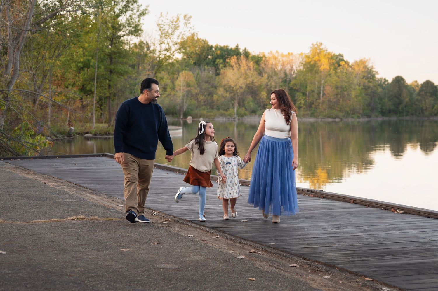 Family walking along a lakeside dock in coordinated navy, cream, and blue outfits for lifestyle family photos.