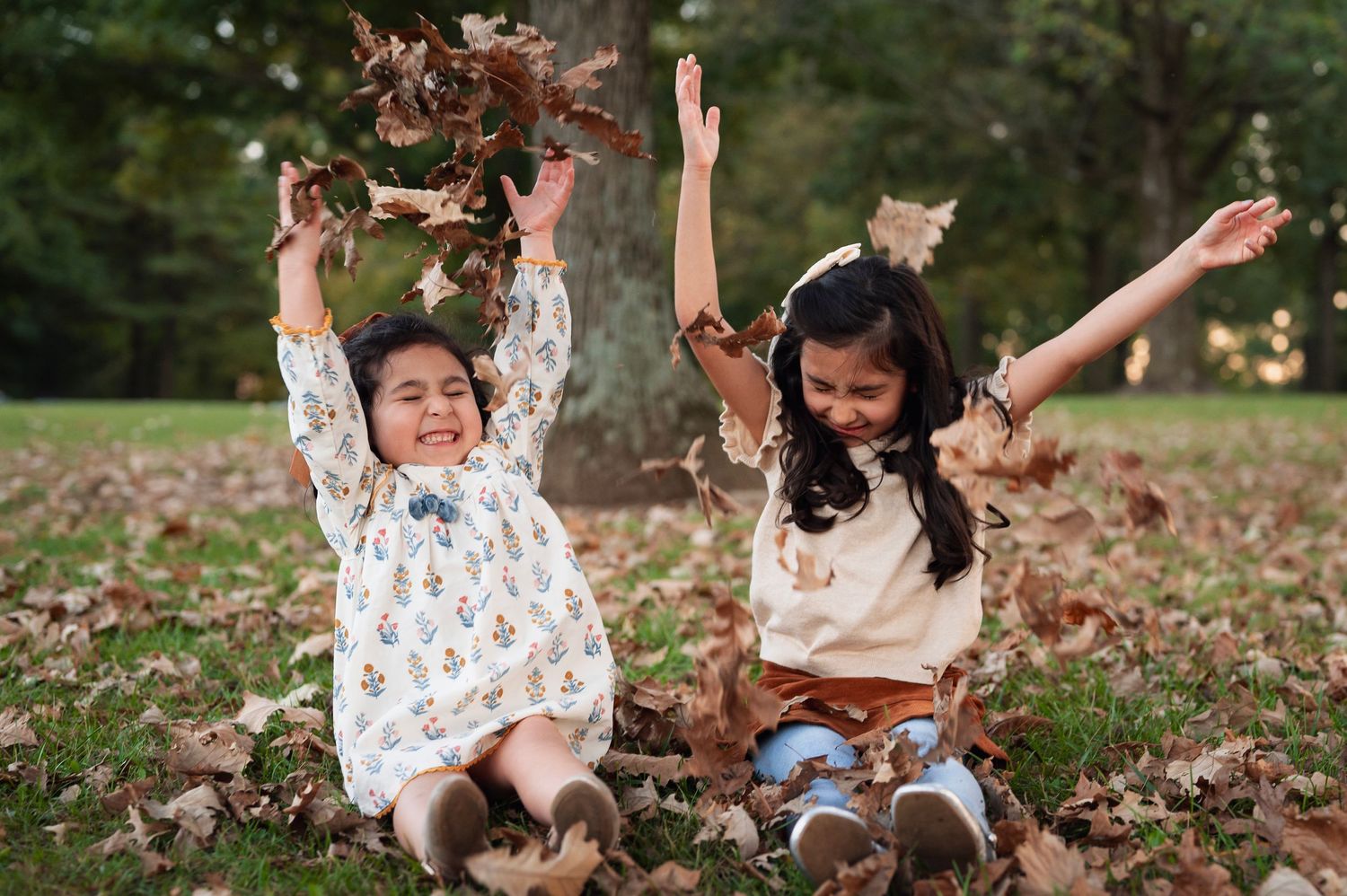 Two young sisters toss dry leaves in the air, laughing and making a joyful mess during their fall family photos in Ohio.