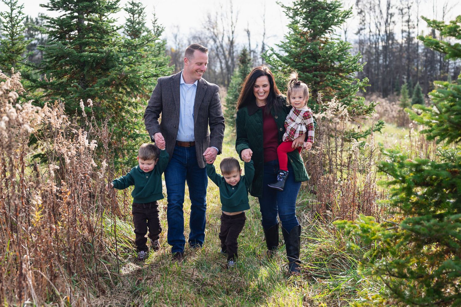 Family walking hand-in-hand through a Christmas tree farm during a winter mini session in central Ohio.