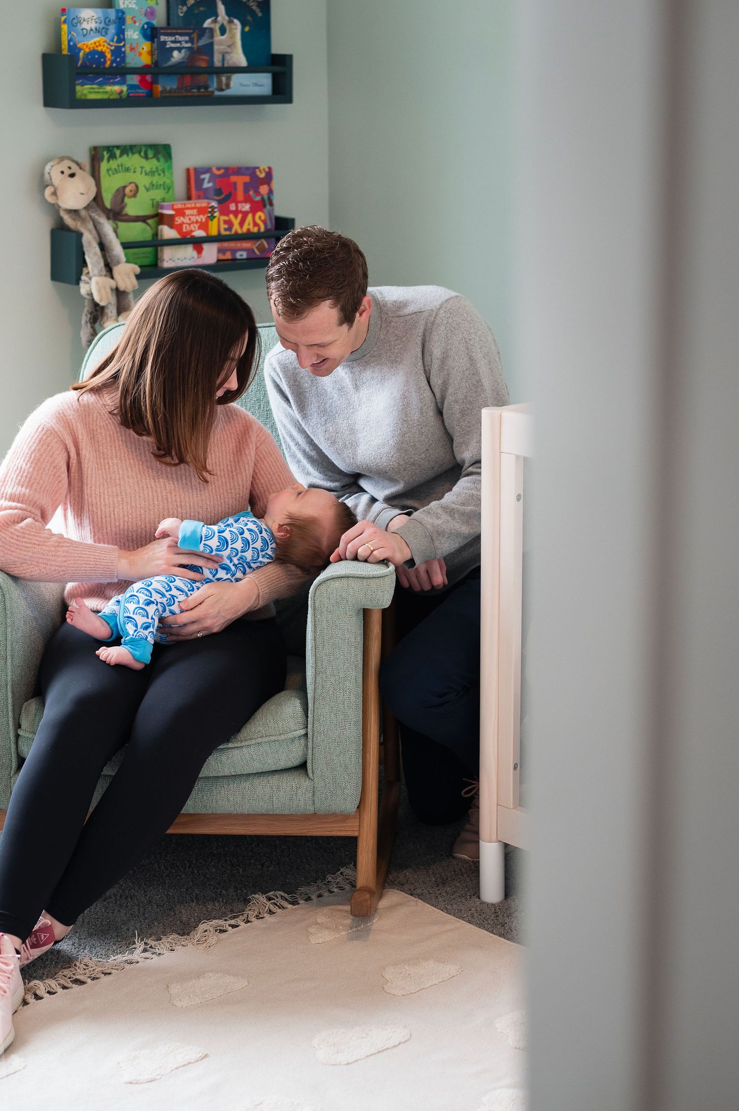 Parents snuggle with their newborn in a cozy nursery, capturing quiet connection during a lifestyle newborn session.