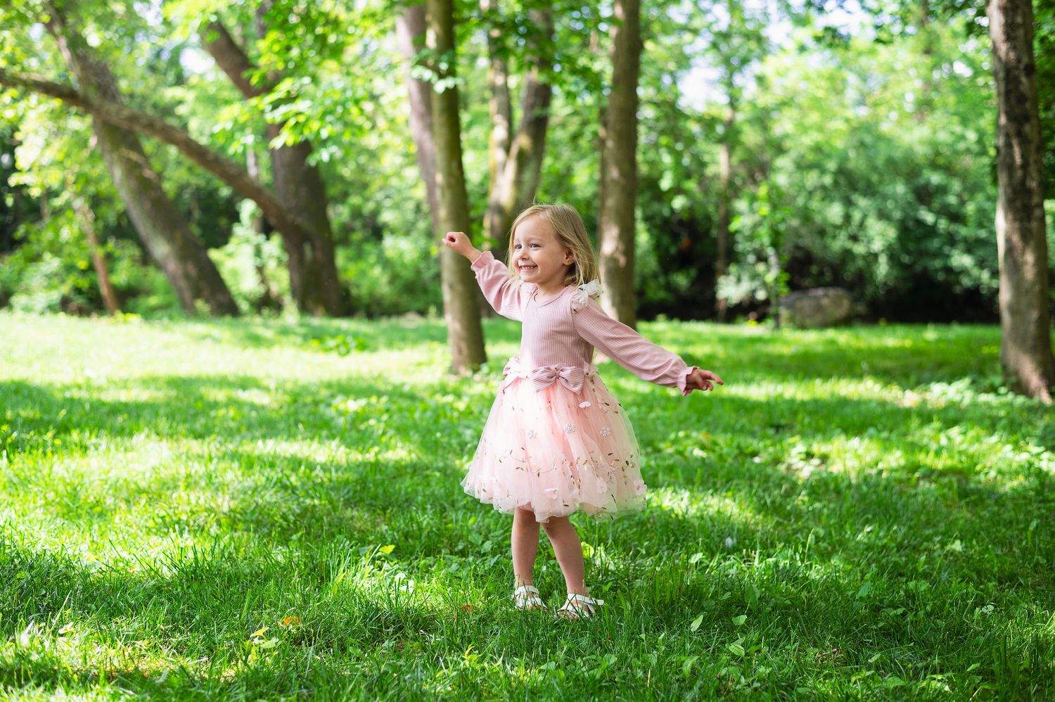 Her pink dress, that big grin, and sunshine through the trees—pure childhood joy on full display