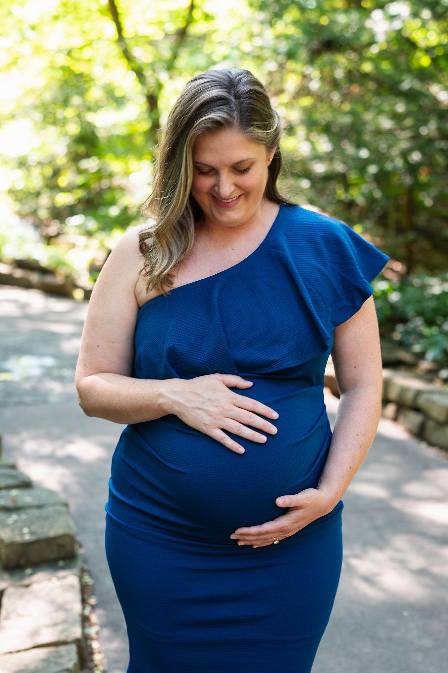 Maternity session at Innis Woods—expecting mom in blue dress smiling down at her belly in lush Westerville park