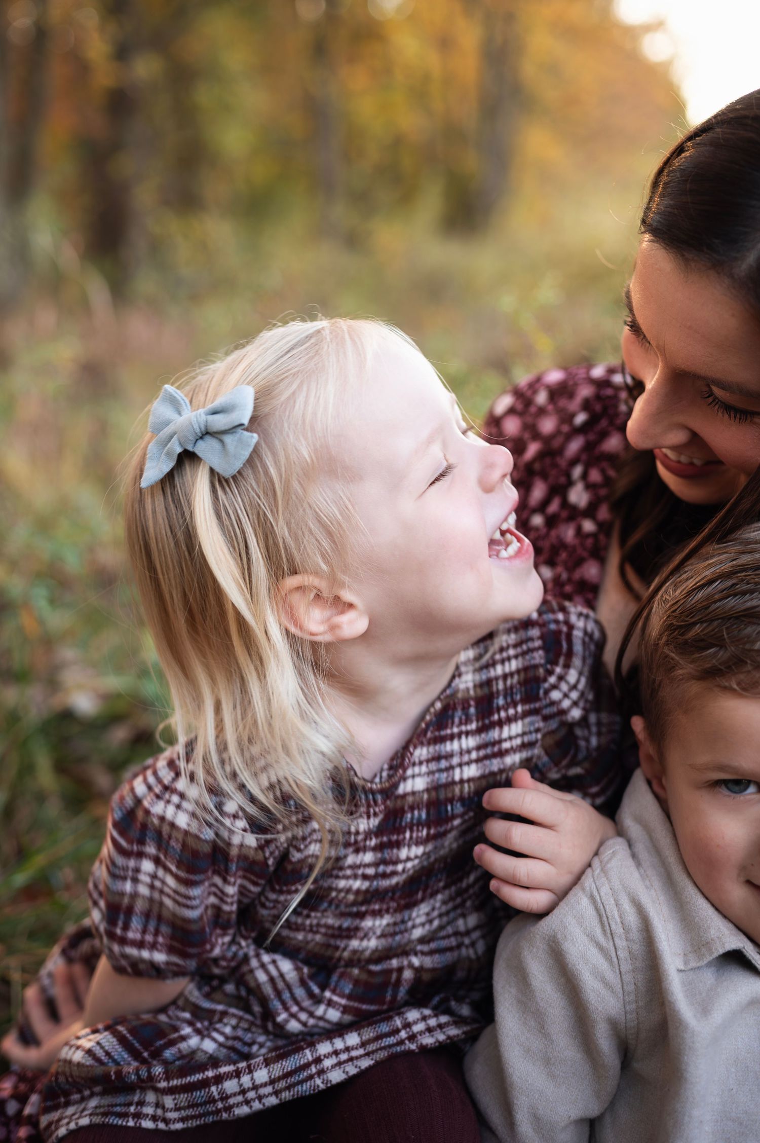 Close-up of a little girl laughing in a plaid dress with a soft fabric bow in her hair, showing how a simple accessory completes her outfit.
