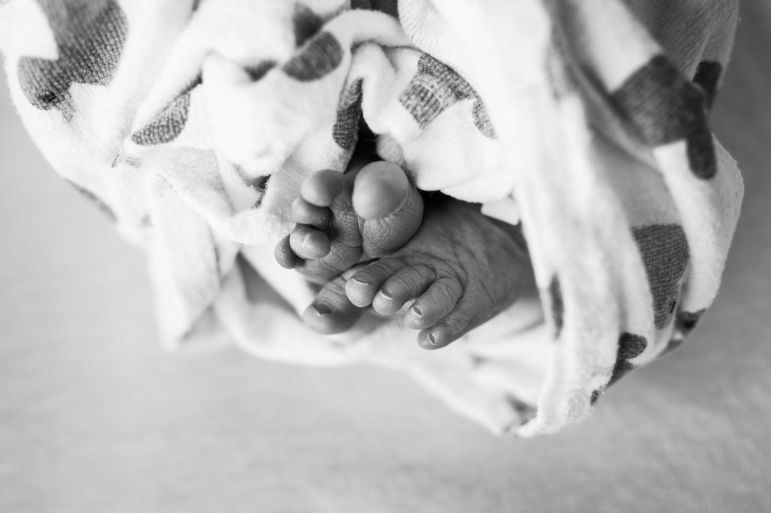 Close-up of newborn baby feet wrapped in a heart-covered blanket, a timeless black-and-white moment from a Fresh 48 session.