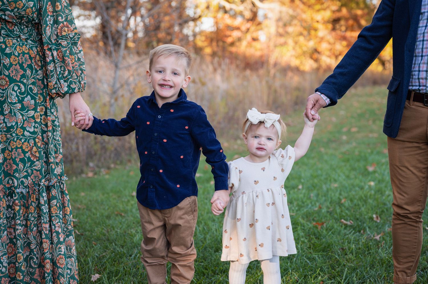 Brother and sister smile while holding hands with parents during a colorful fall photo session.