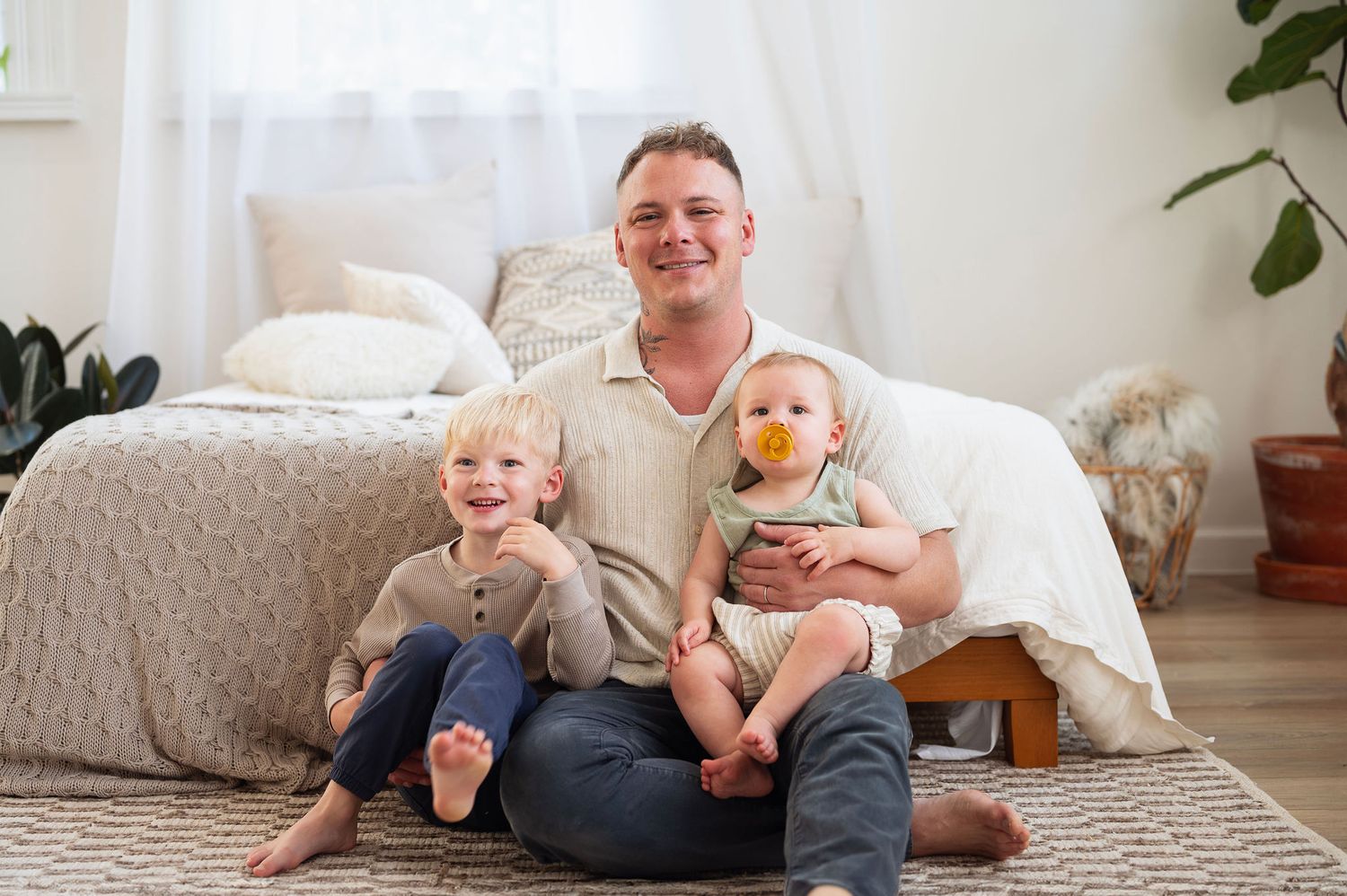 Natural light family photography session with dad and two young boys, captured in a cozy, neutral-toned studio setting.