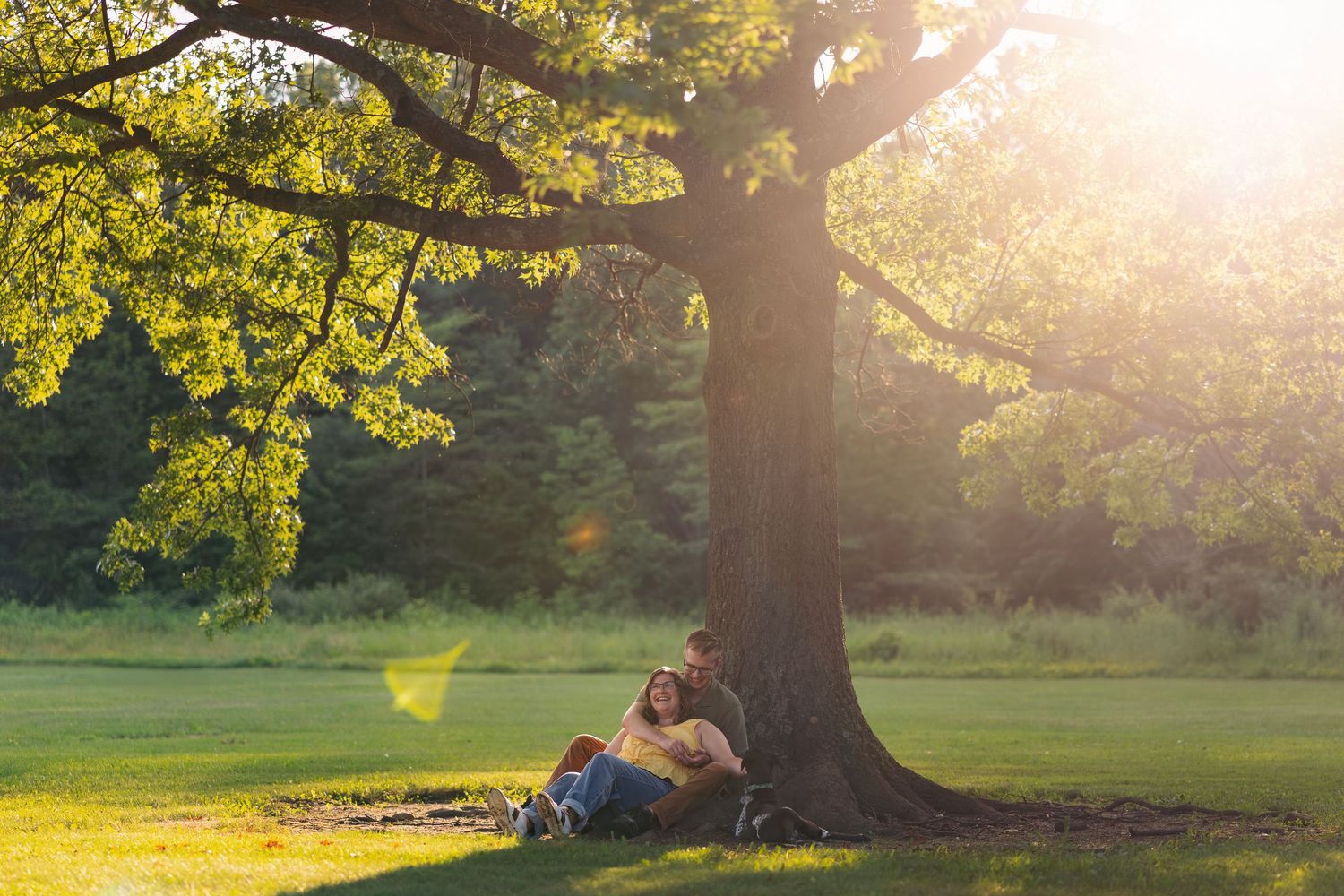 Couple sitting under a large oak tree with dog at Sharon Woods during golden hour