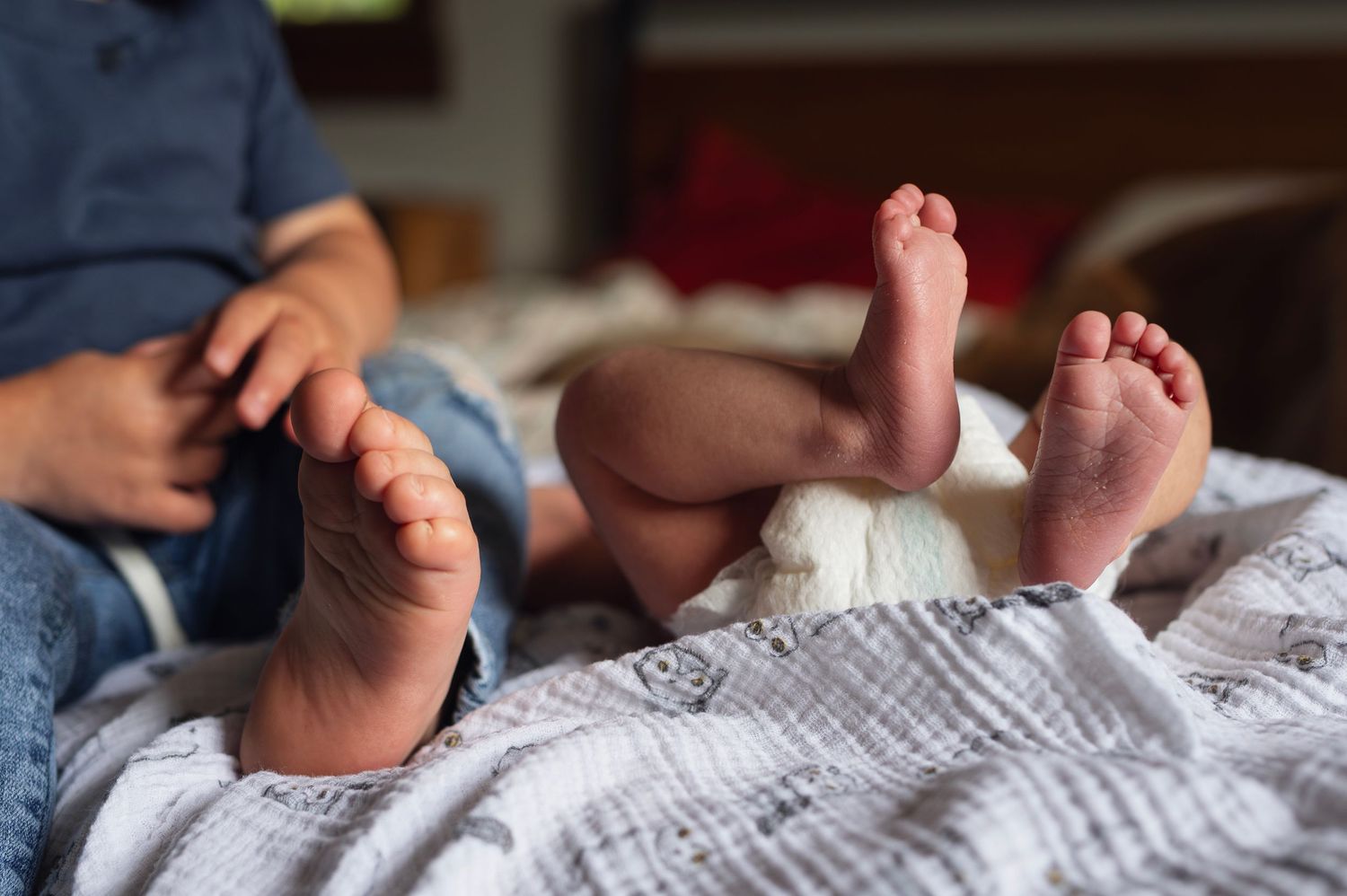 Sibling and newborn toes side by side on a soft blanket during a relaxed in-home newborn session.