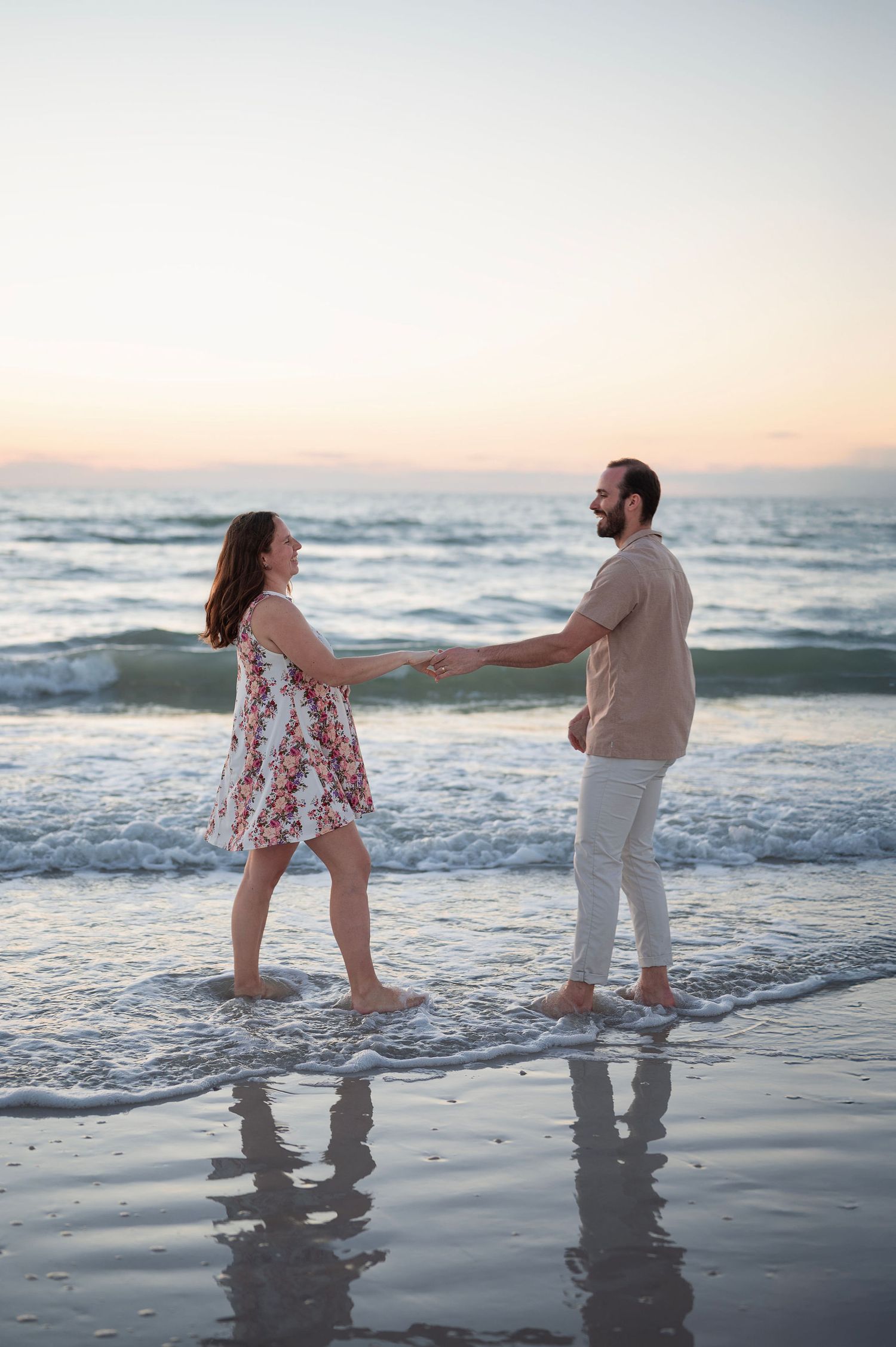 Playful maternity photo of a couple laughing in the surf at sunset—joyful, candid portraits with a lifestyle photographer’s touch.