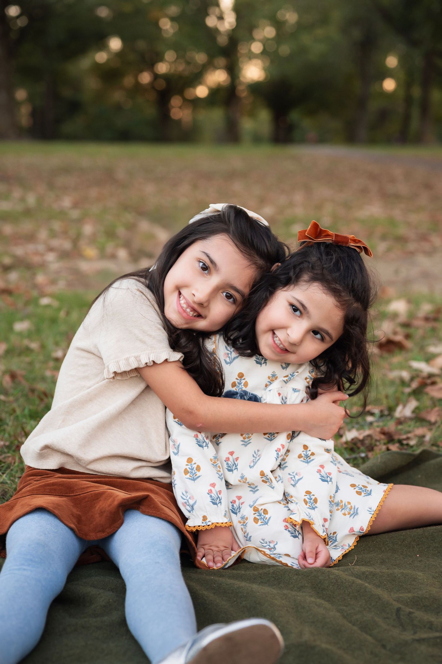 Sisters snuggle on a green blanket, big sister wrapping little sister in a hug during their playful Westerville family session.