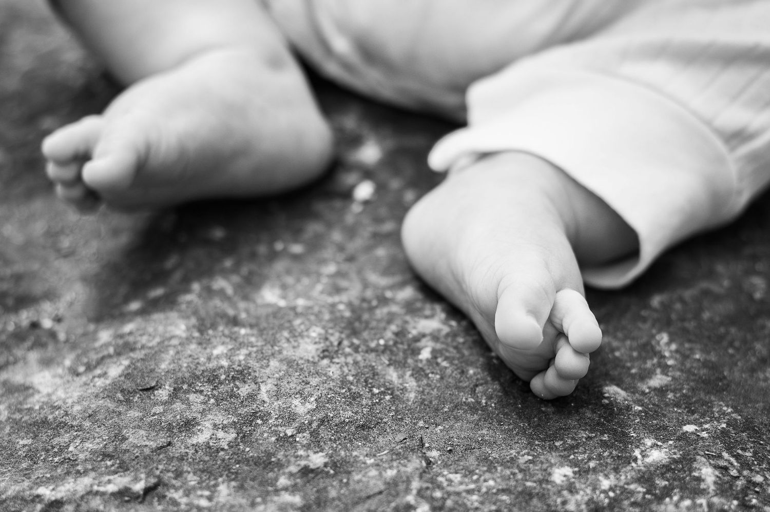 Black and white close-up of tiny baby feet on textured stone, a timeless newborn detail full of softness and story.