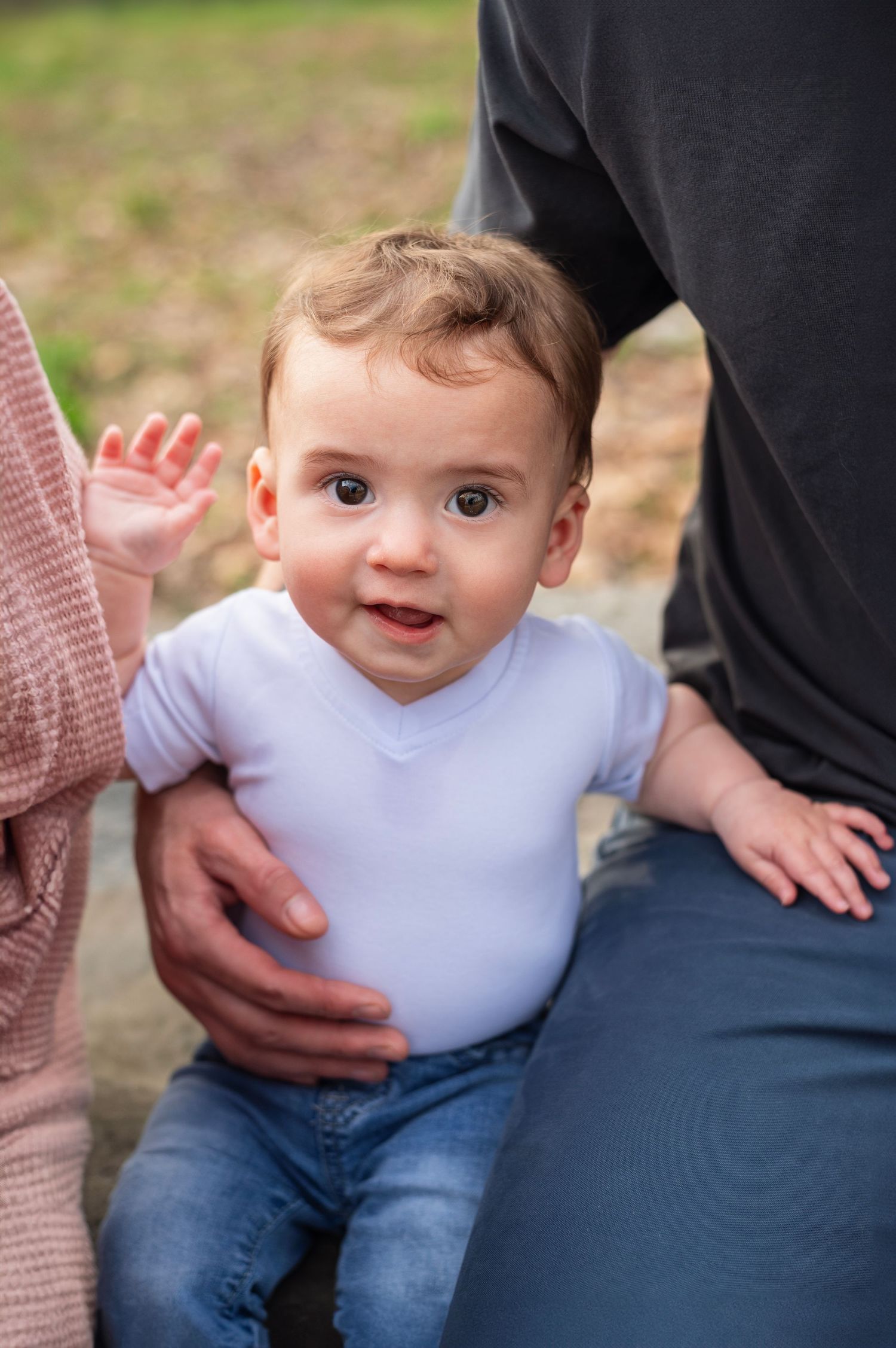 Westerville newborn photographer photo of a baby smiling in a white onesie while sitting with parents.