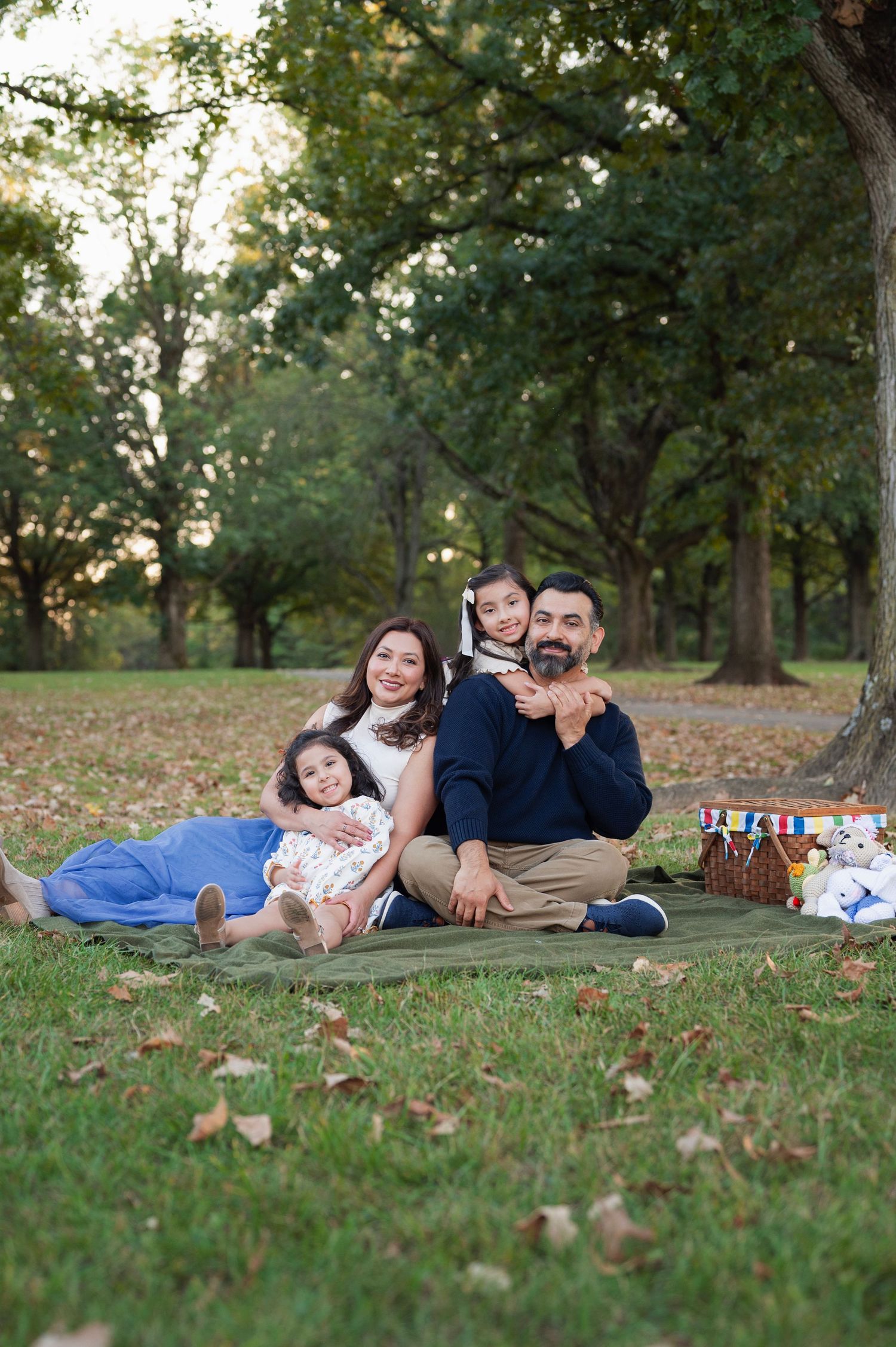 Fall family of four lounges on a green blanket with a picnic basket and handmade stuffed animals during Westerville family photos.