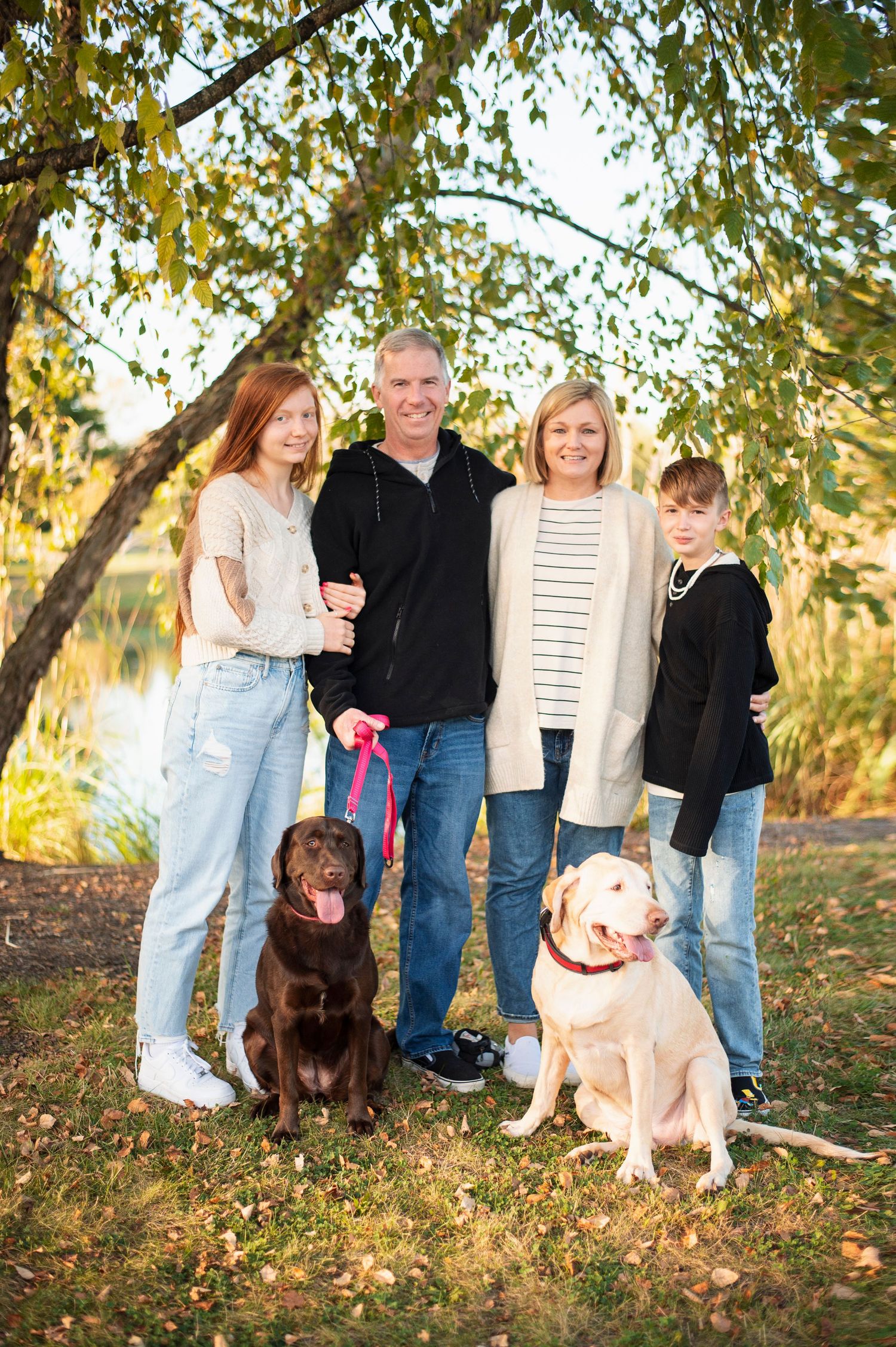 Family with two teens and dogs posing under tree at sunset, Westerville fall family photography.
