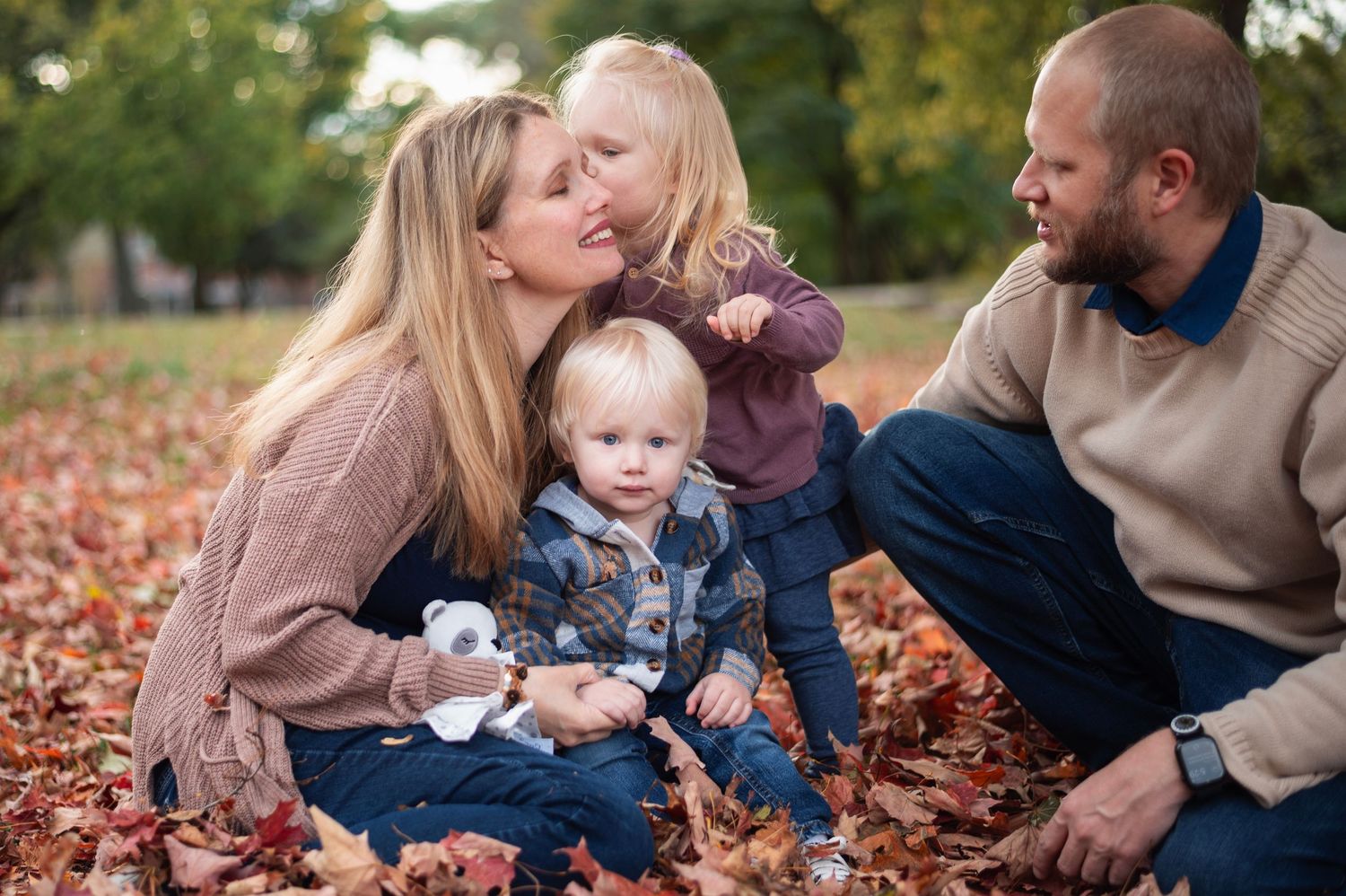 Mom smiling as daughter kisses her cheek in autumn leaves during Columbus family photo session