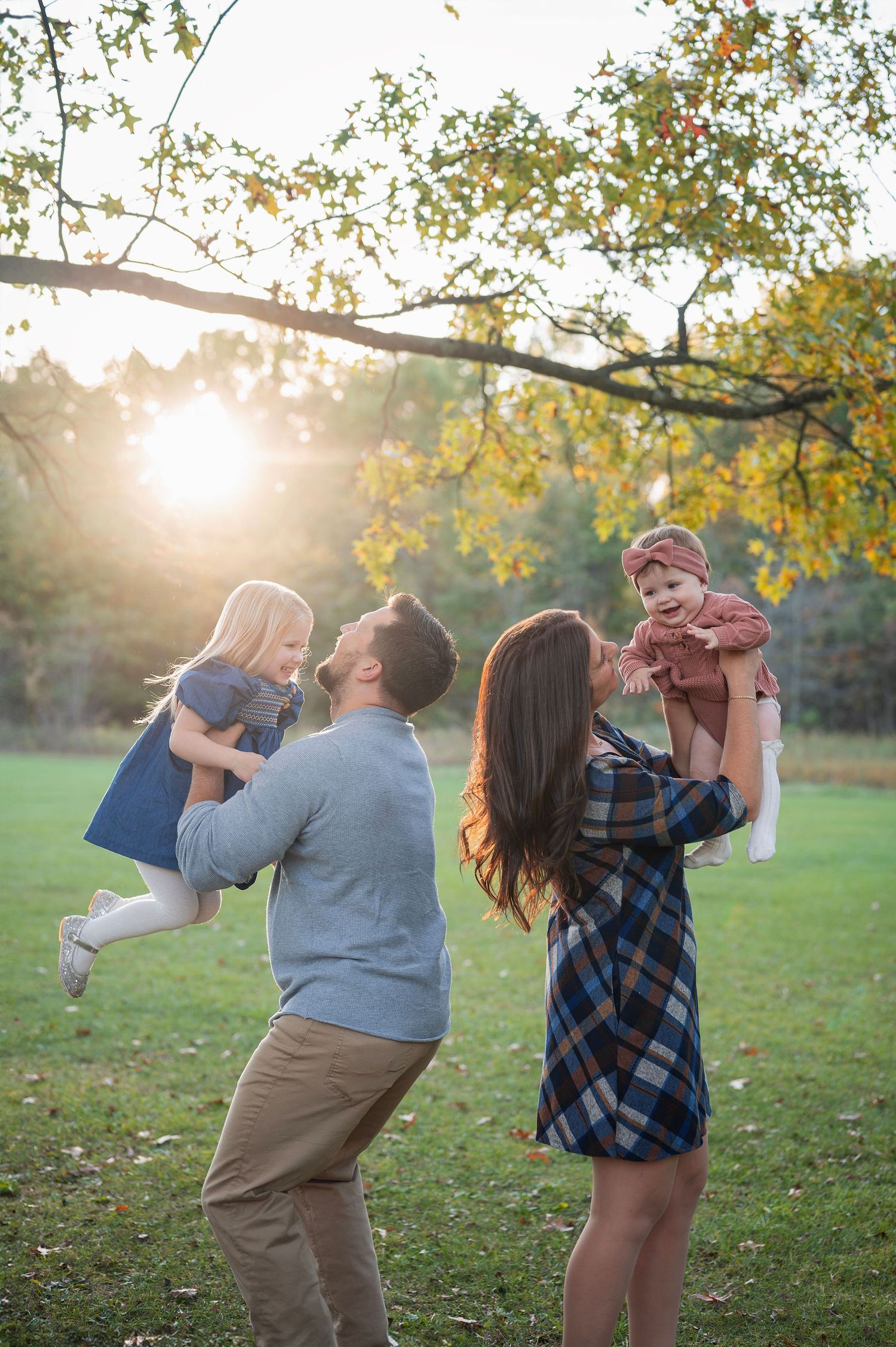Golden hour fall family photo in Westerville park—parents lifting daughters with joy and laughter