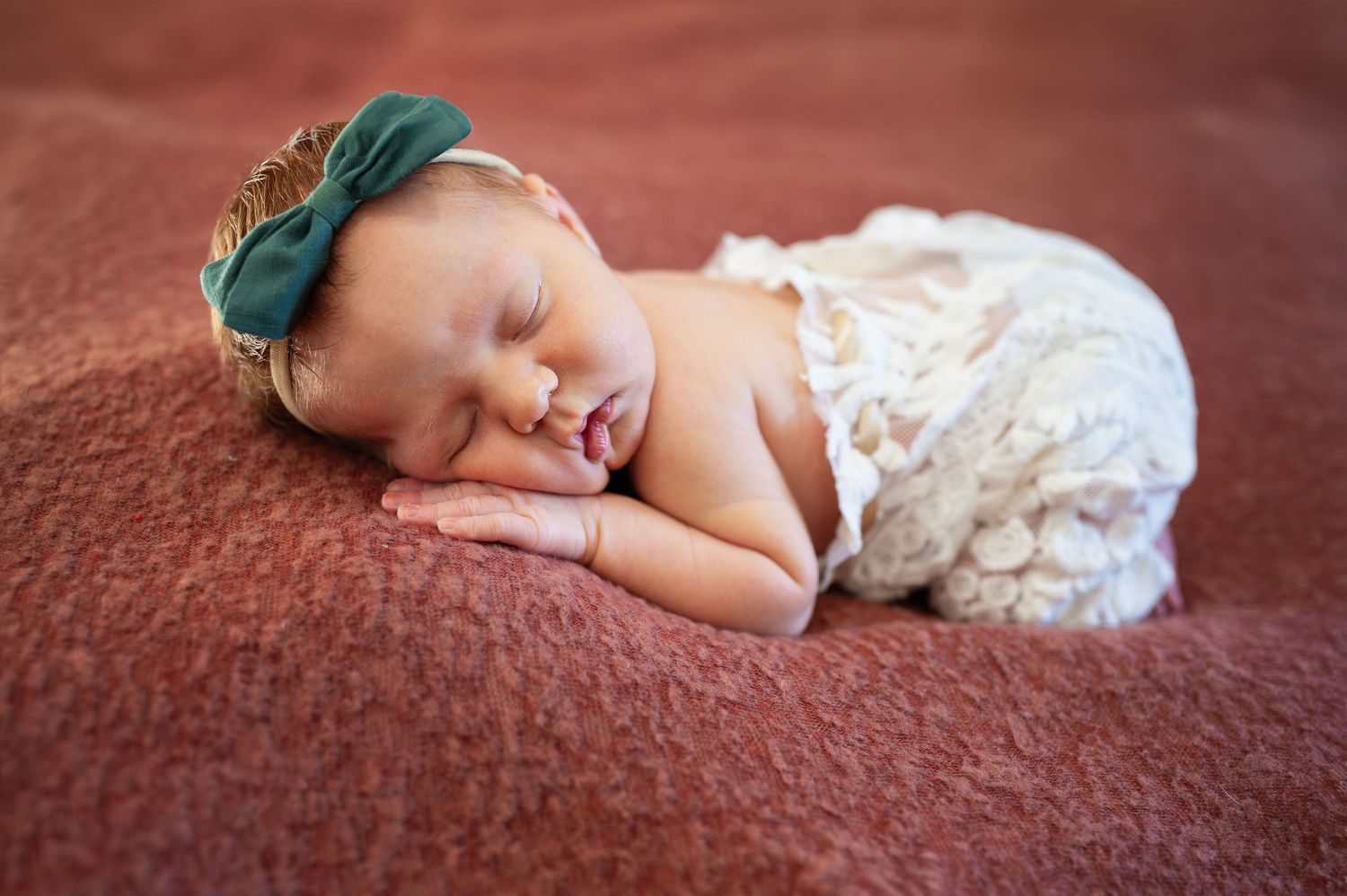 Newborn girl sleeping peacefully in lace wrap and bow—studio newborn session in Columbus area