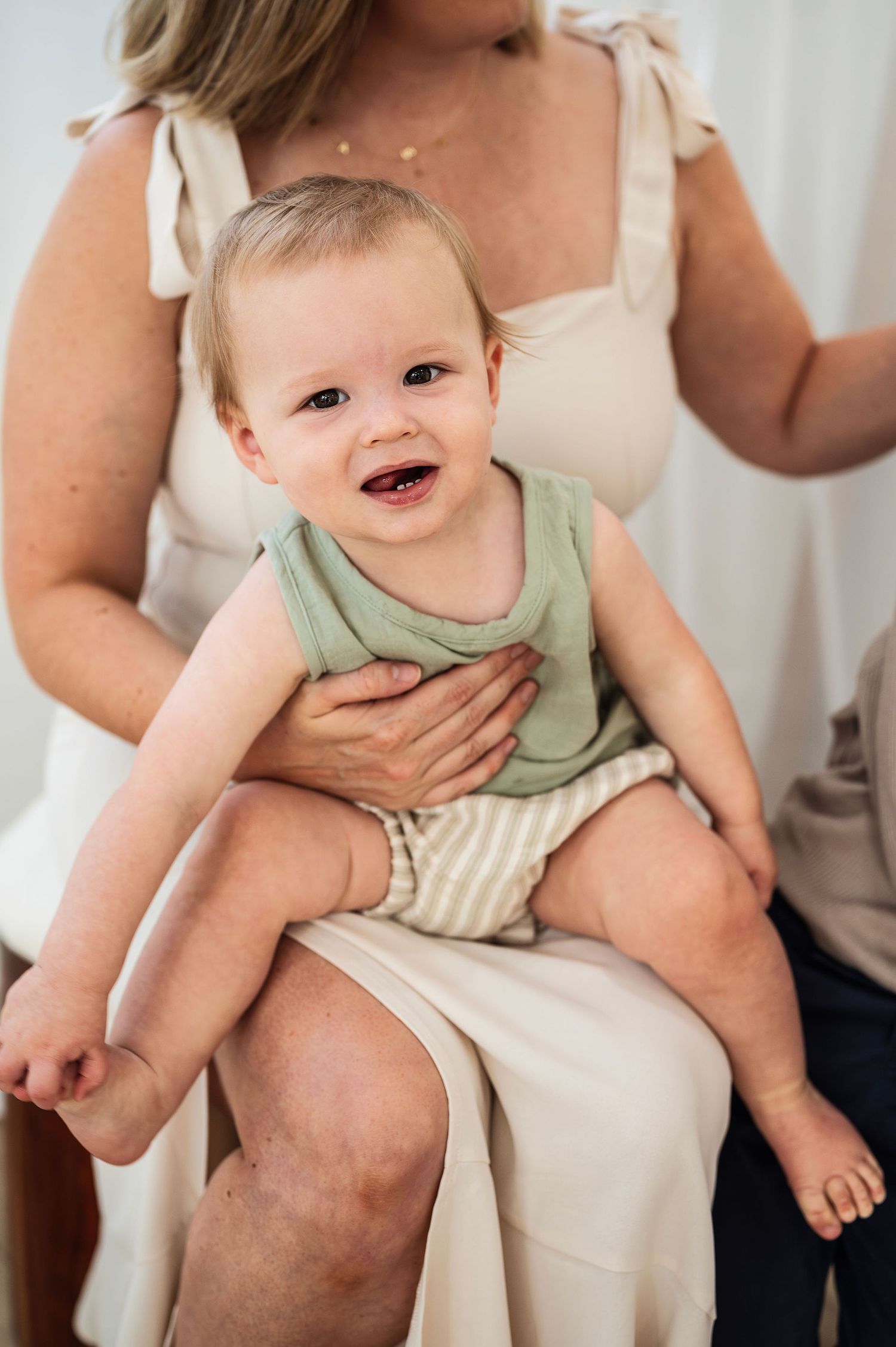 Milestone photography session with a happy toddler smiling in natural light, cradled in mama’s arms in a neutral-toned studio.