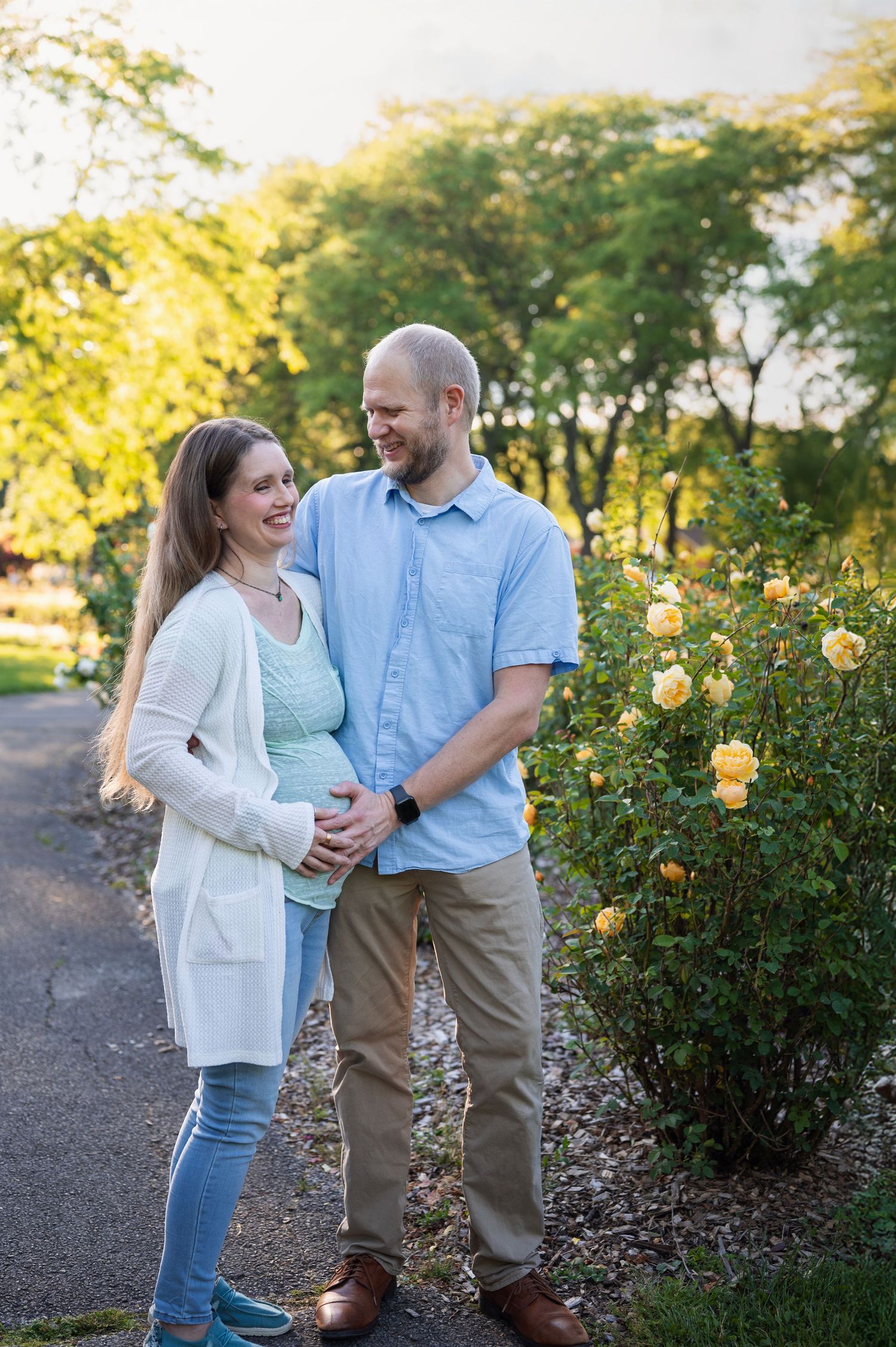 Expecting couple smiling together near yellow rose bushes at Franklin Park maternity session