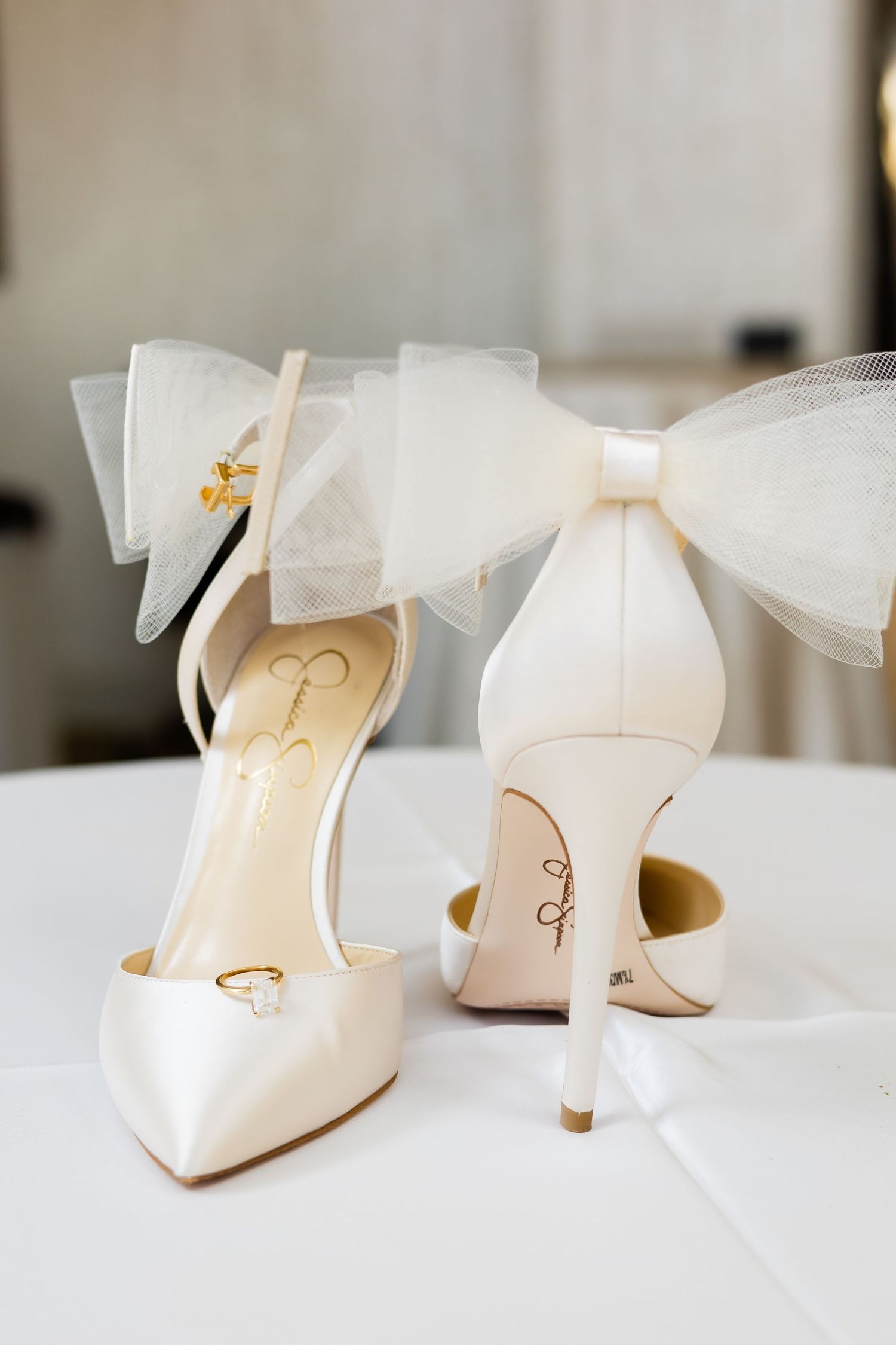 Ivory bridal heels with tulle bow detail displayed on white table for wedding day.