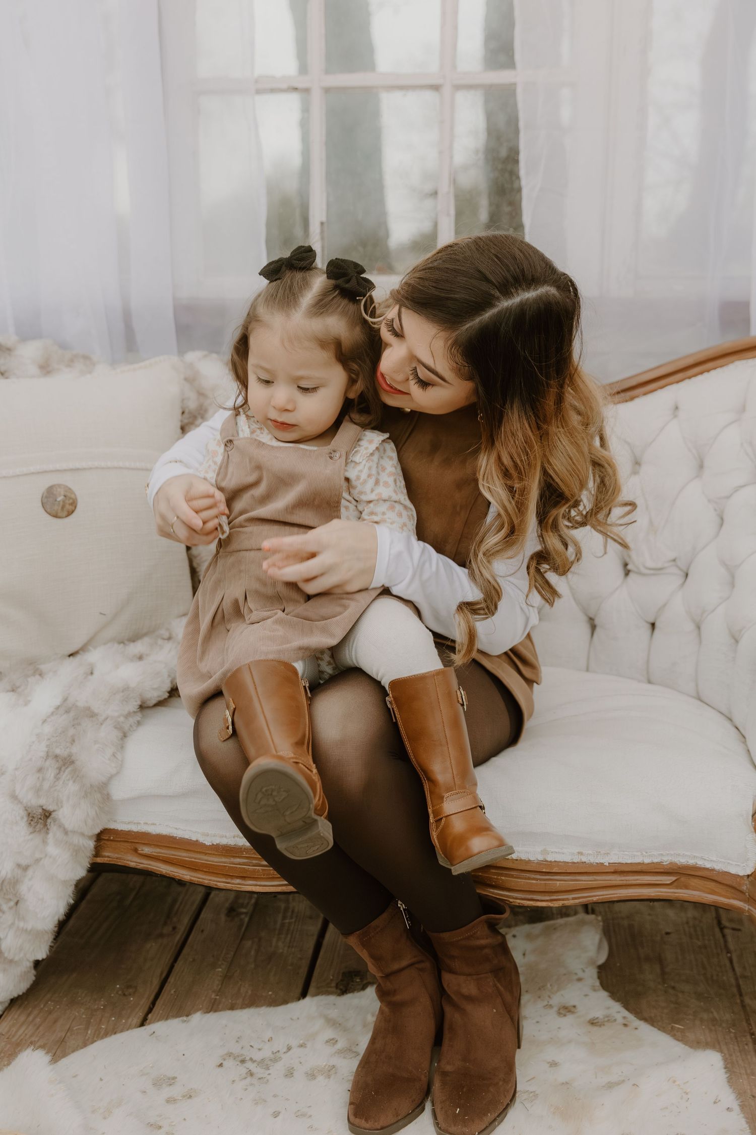 A tender moment shared between parent and child sitting on a tufted couch wearing matching brown boots.