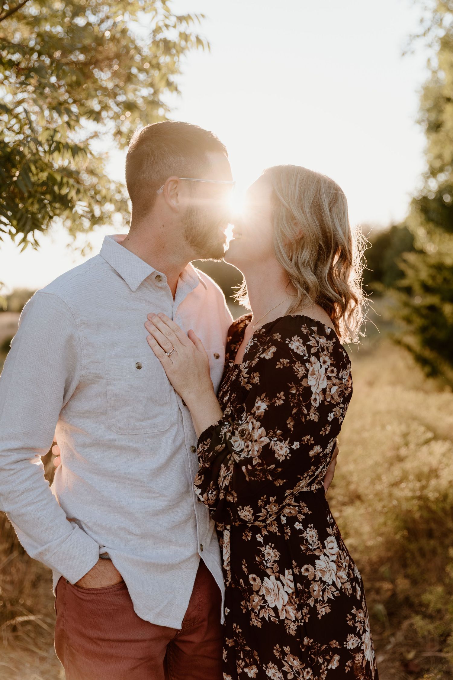 A romantic sunset engagement photo with a couple embracing outdoors in golden light.