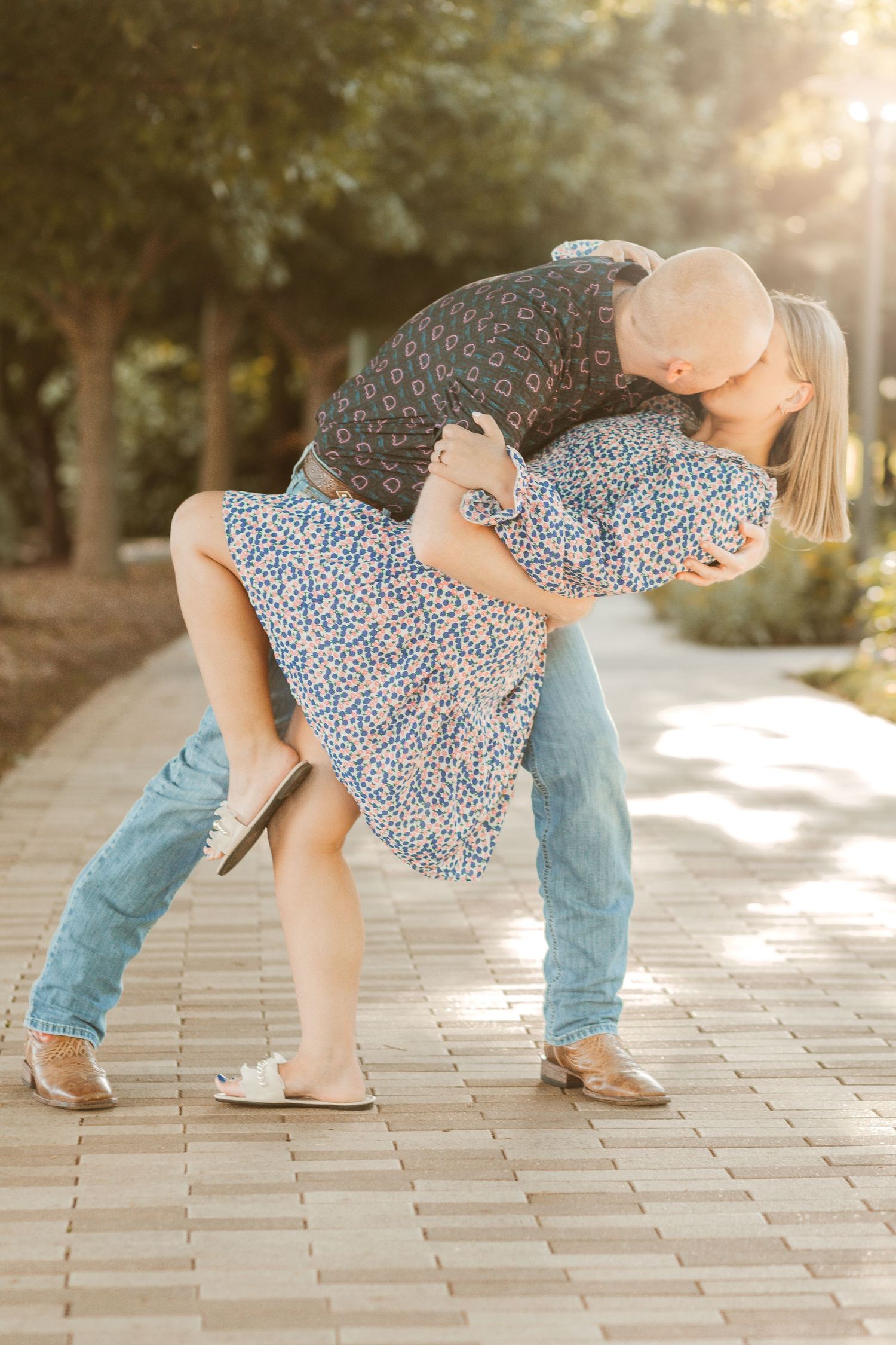 Romantic dip pose on brick pathway during sunset with trees in background.