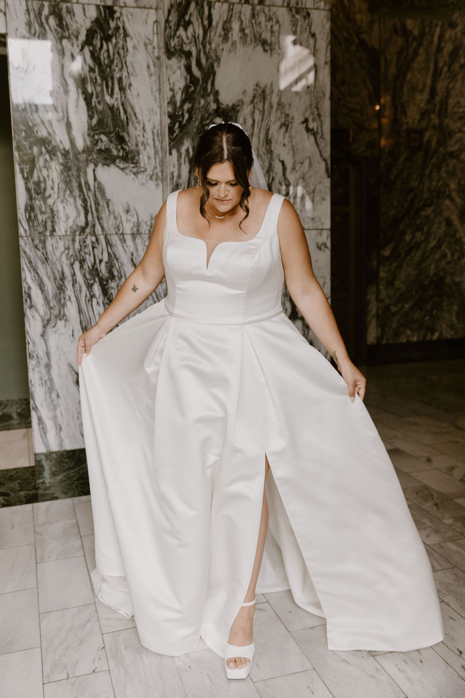 A bride in a modern white wedding gown with a sweetheart neckline showcases her dress on a marble-patterned floor.