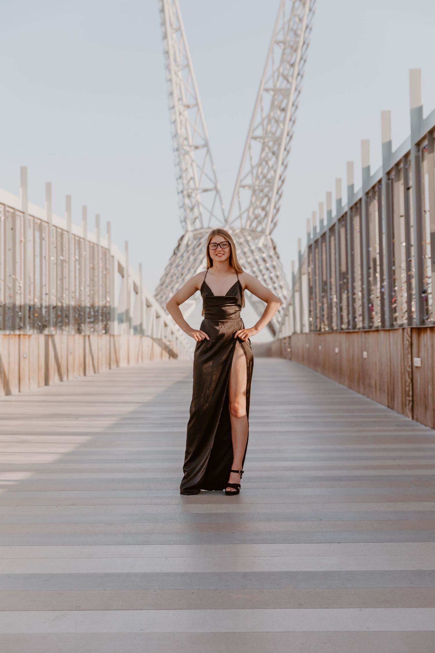 Person in flowing black dress poses on an architectural bridge walkway with geometric white railings and pillars.