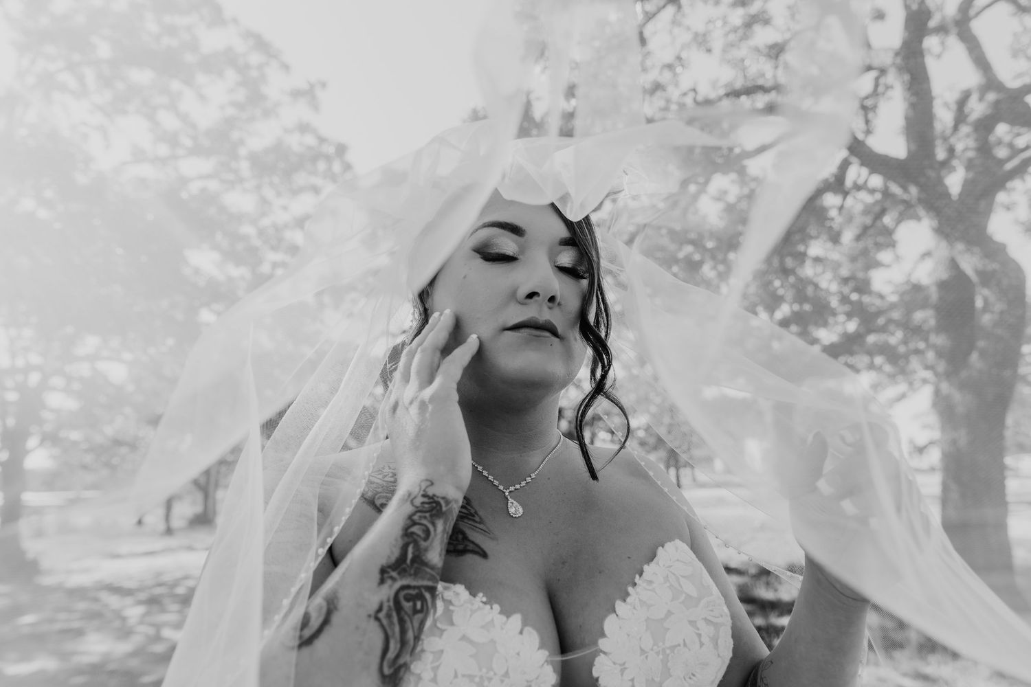 Dreamy black and white portrait of a bride in a strapless gown with flowing veil and closed eyes.